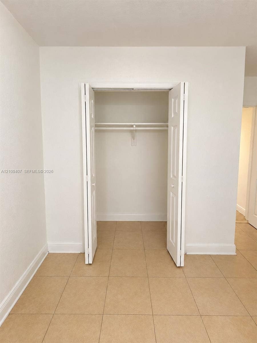 Interior space featuring neutral-toned tile flooring and a built-in closet with white six-panel bifold doors, an interior shelf, and a hanging rod