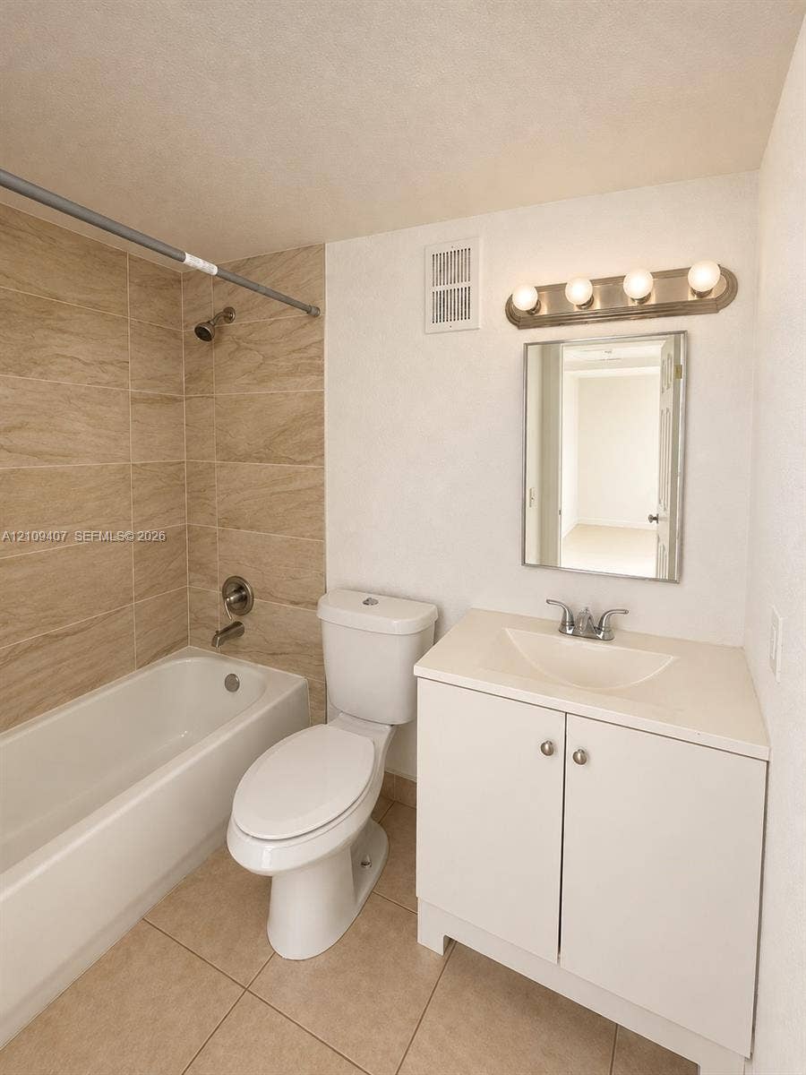 Bathroom featuring a white vanity cabinet with an integrated sink, neutral stone-finish floor tiling, and a shower-tub combination finished with textured wall tile