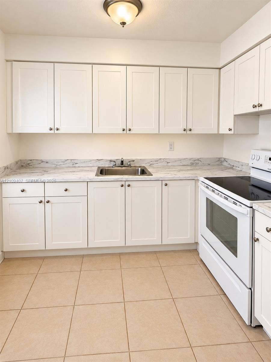 Kitchen featuring white shaker-style cabinetry, stone-pattern laminate countertops, a stainless steel sink with a dual-handle faucet, white electric range, and ceramic tile flooring