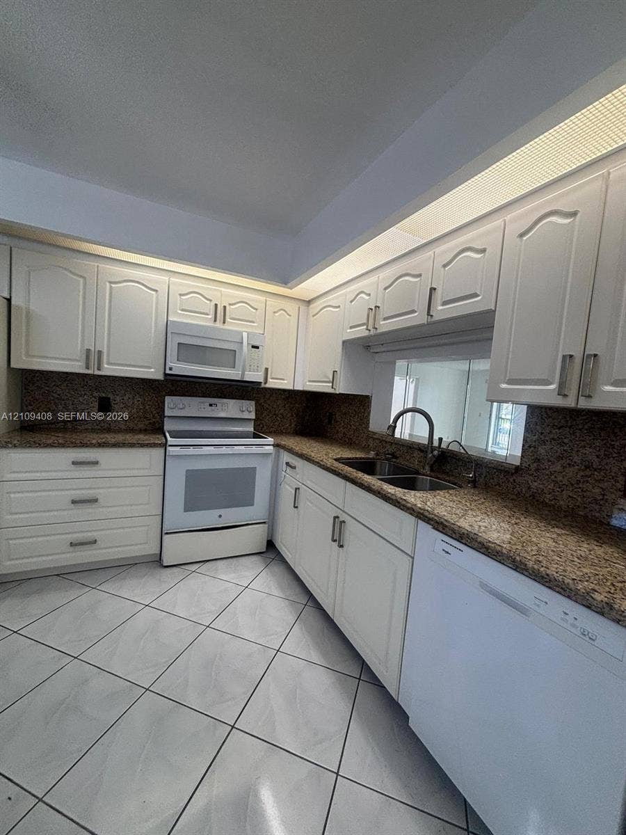 12600 SW 5th Court, #208L, Pembroke Pines, Pembroke Pines, FL 33027 Kitchen featuring white cabinetry, stone-finish countertops, tile flooring, integrated over-range microwave, and a dual-basin sink with a gooseneck faucet