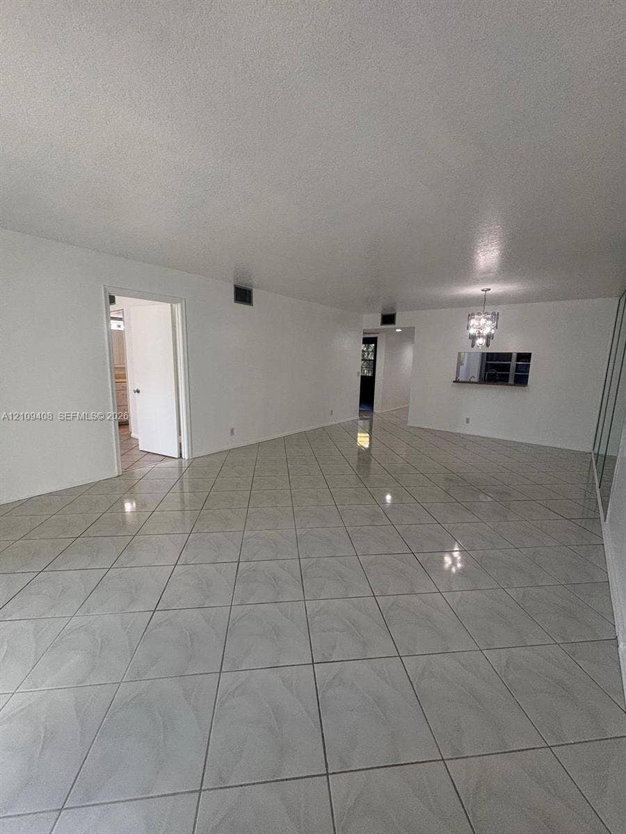 12600 SW 5th Court, #208L, Pembroke Pines, Pembroke Pines, FL 33027 Spacious interior featuring large-format tile flooring, a built-in pass-through window with an attached pendant light fixture, and mirrored wall accents