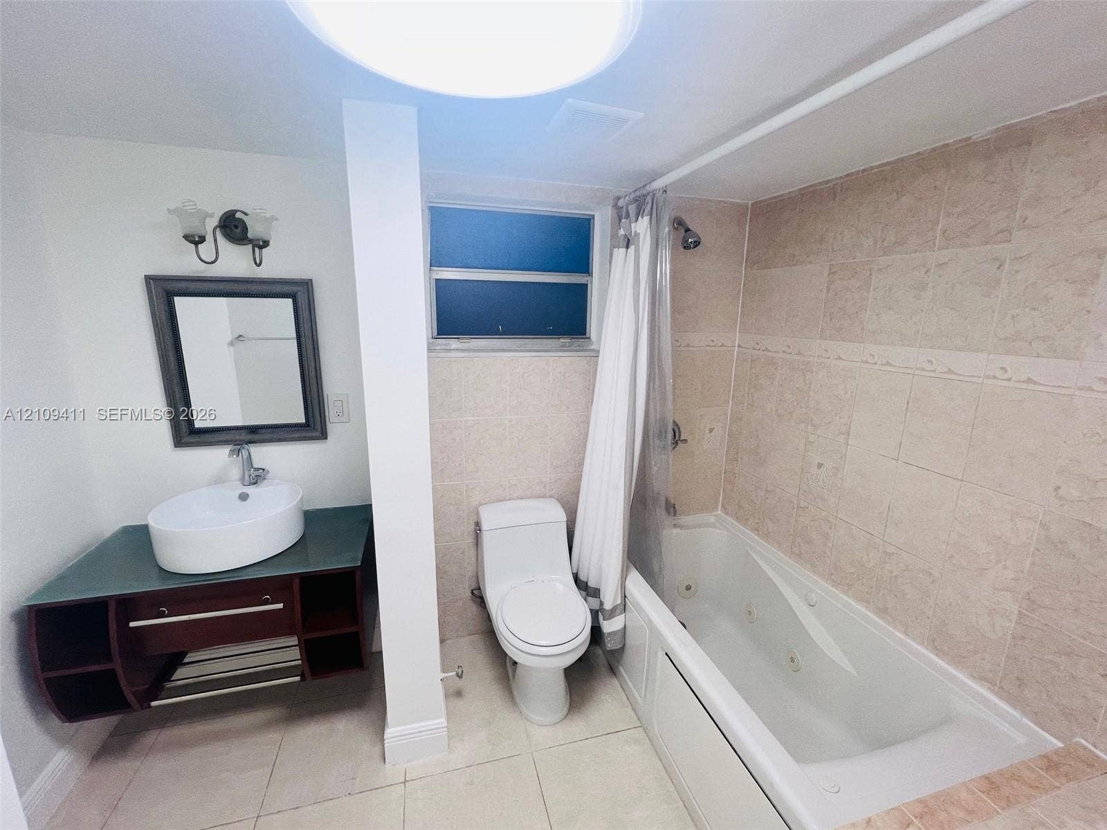 Bathroom featuring a floating vanity with a vessel sink, a jetted soaking tub, tiled shower surround, and a wall-mounted light fixture