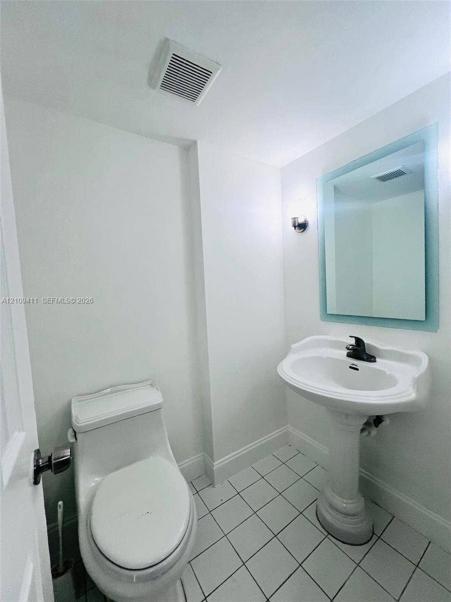 Pedestal sink with a dark-finish faucet, wall-mounted backlit mirror, and ceramic tile flooring