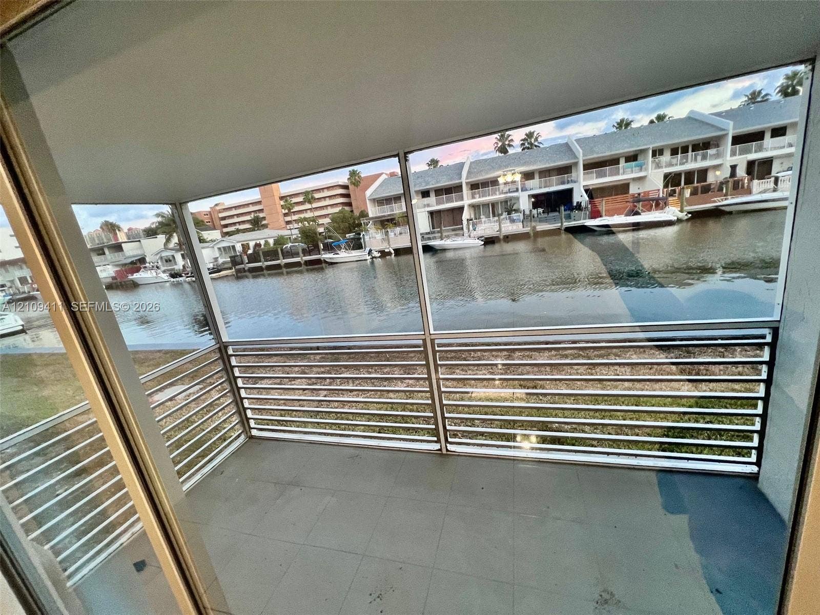 Covered balcony featuring tile flooring and horizontal metal railings overlooking a canal with bulkhead docks