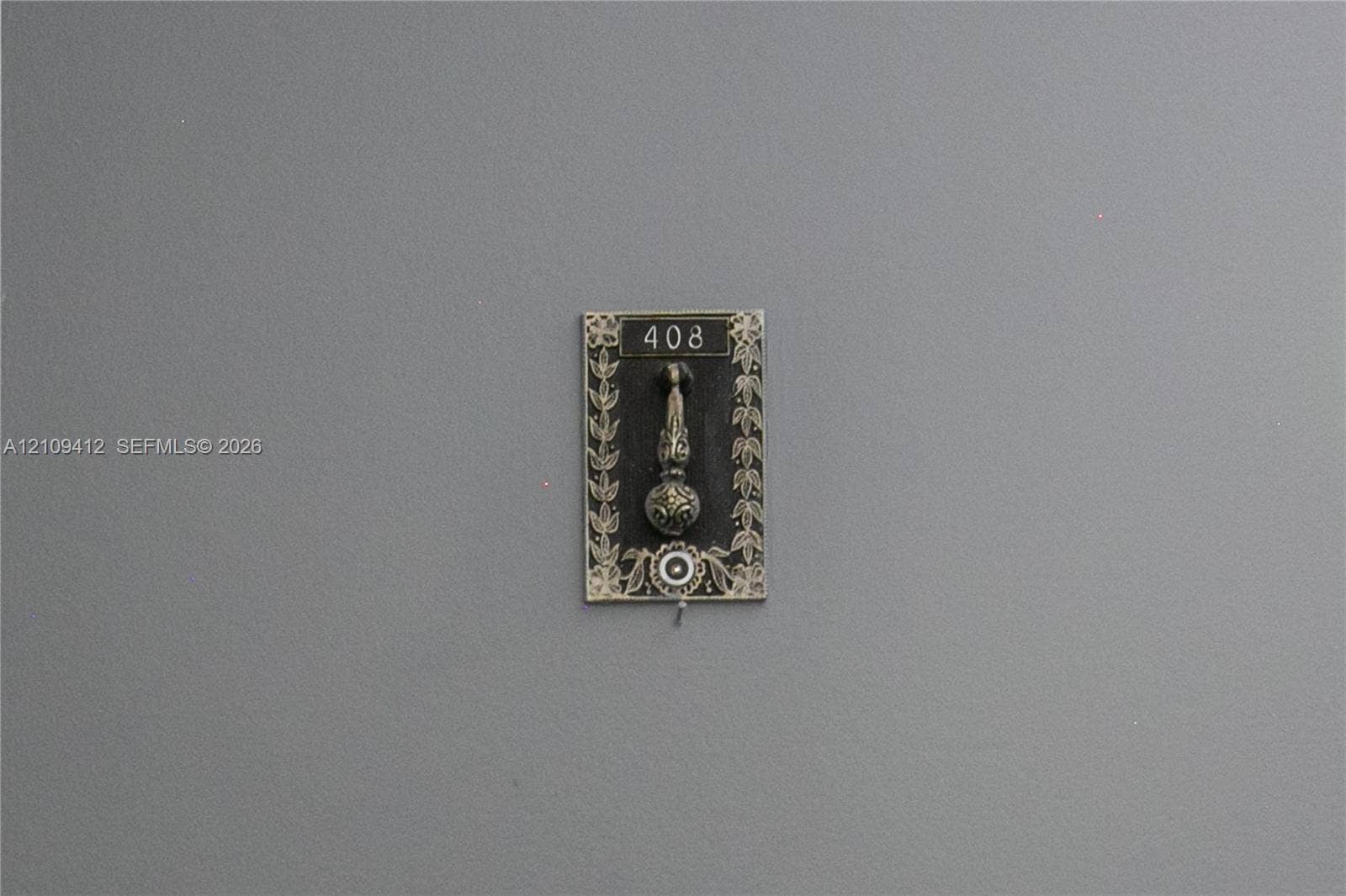 137 Golden Isles Drive, #408, Hallandale Beach, FL 33009 Decorative metal door knocker featuring an ornate floral border, engraved numbering, and a circular accent detail