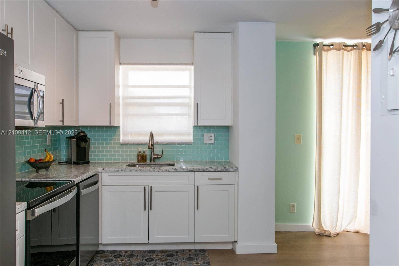 137 Golden Isles Drive, #408, Hallandale Beach, FL 33009 Kitchen featuring white shaker-style cabinetry, light-toned stone-finish countertops, stainless steel appliances, and a blue subway tile backsplash