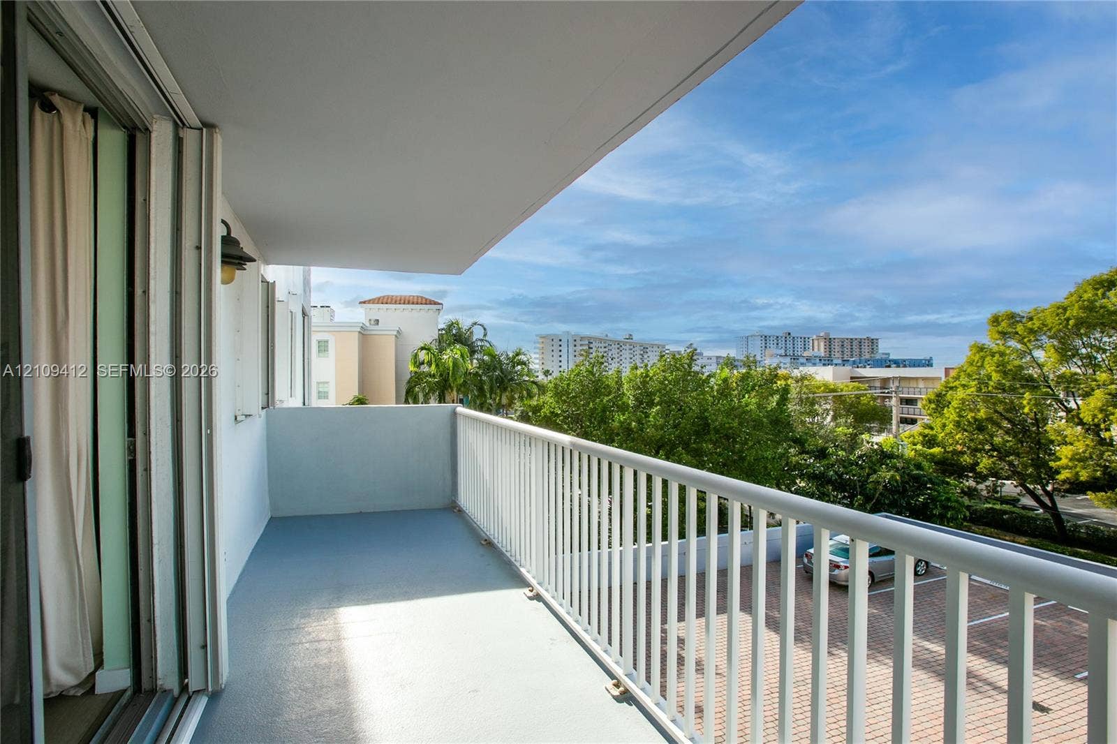 137 Golden Isles Drive, #408, Hallandale Beach, FL 33009 Covered outdoor balcony featuring a solid surface floor, white metal railing, and wall-mounted exterior light fixture