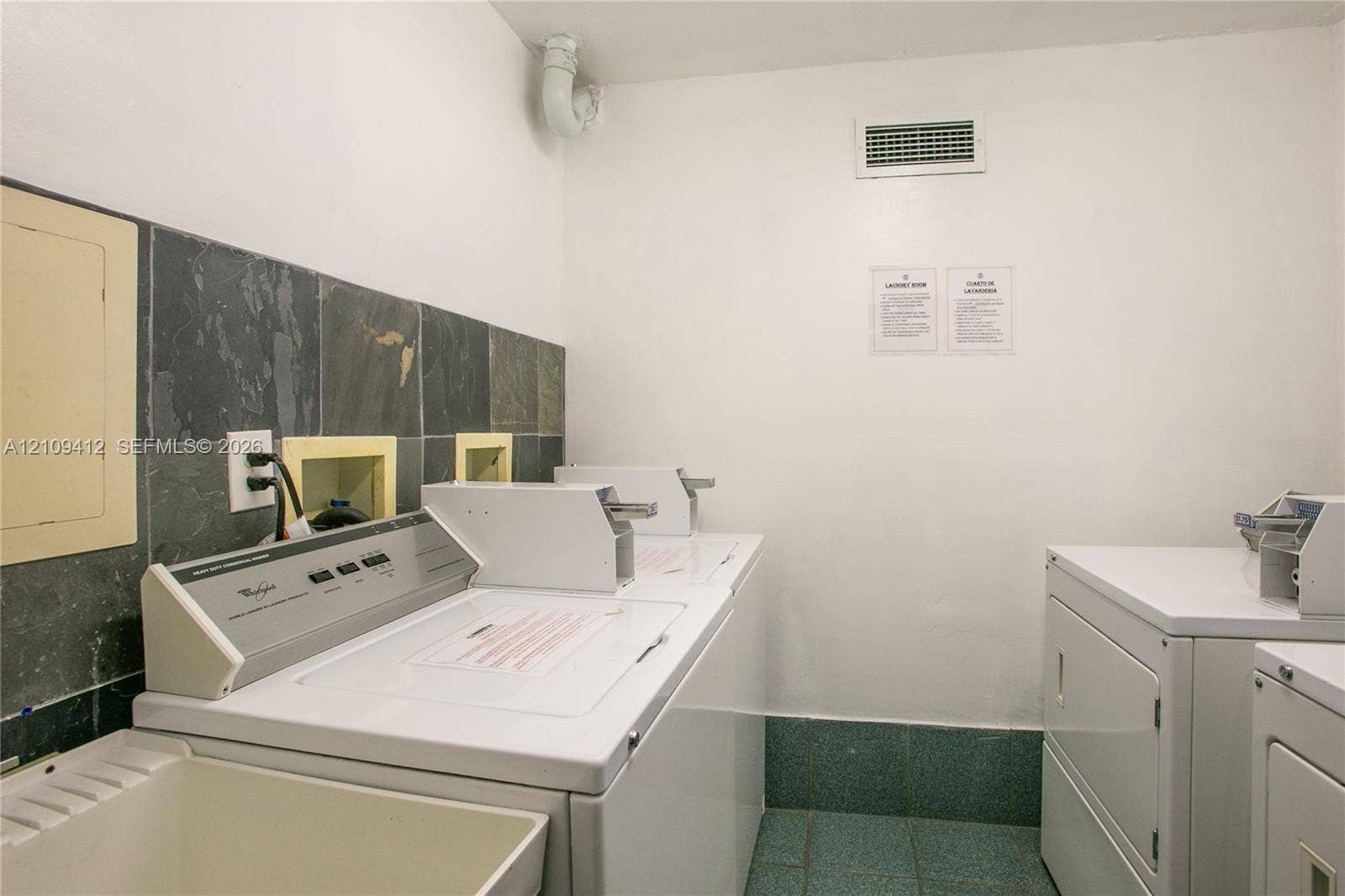 137 Golden Isles Drive, #408, Hallandale Beach, FL 33009 Laundry area featuring tile flooring, stone wall backsplash, and a utility sink
