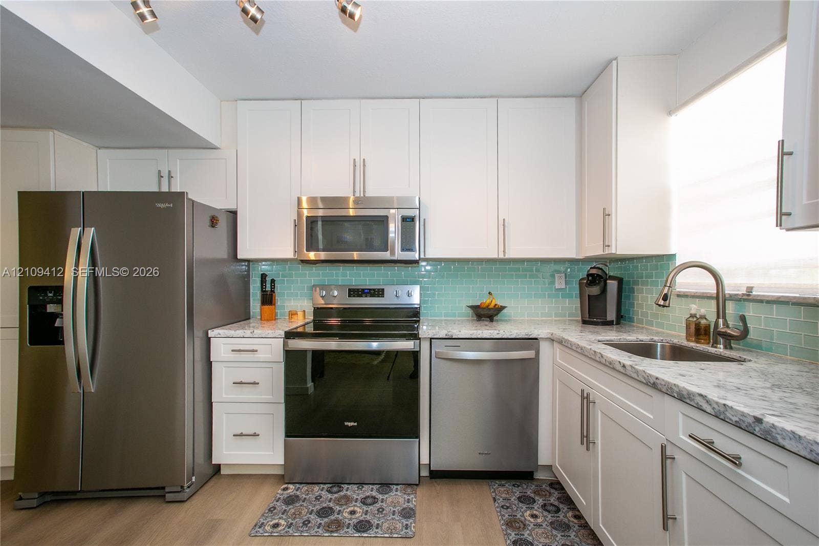 137 Golden Isles Drive, #408, Hallandale Beach, FL 33009 Kitchen featuring white shaker-style cabinetry, stainless steel appliances, speckled stone-finish countertops, a light blue glass subway tile backsplash, and wood-finish flooring