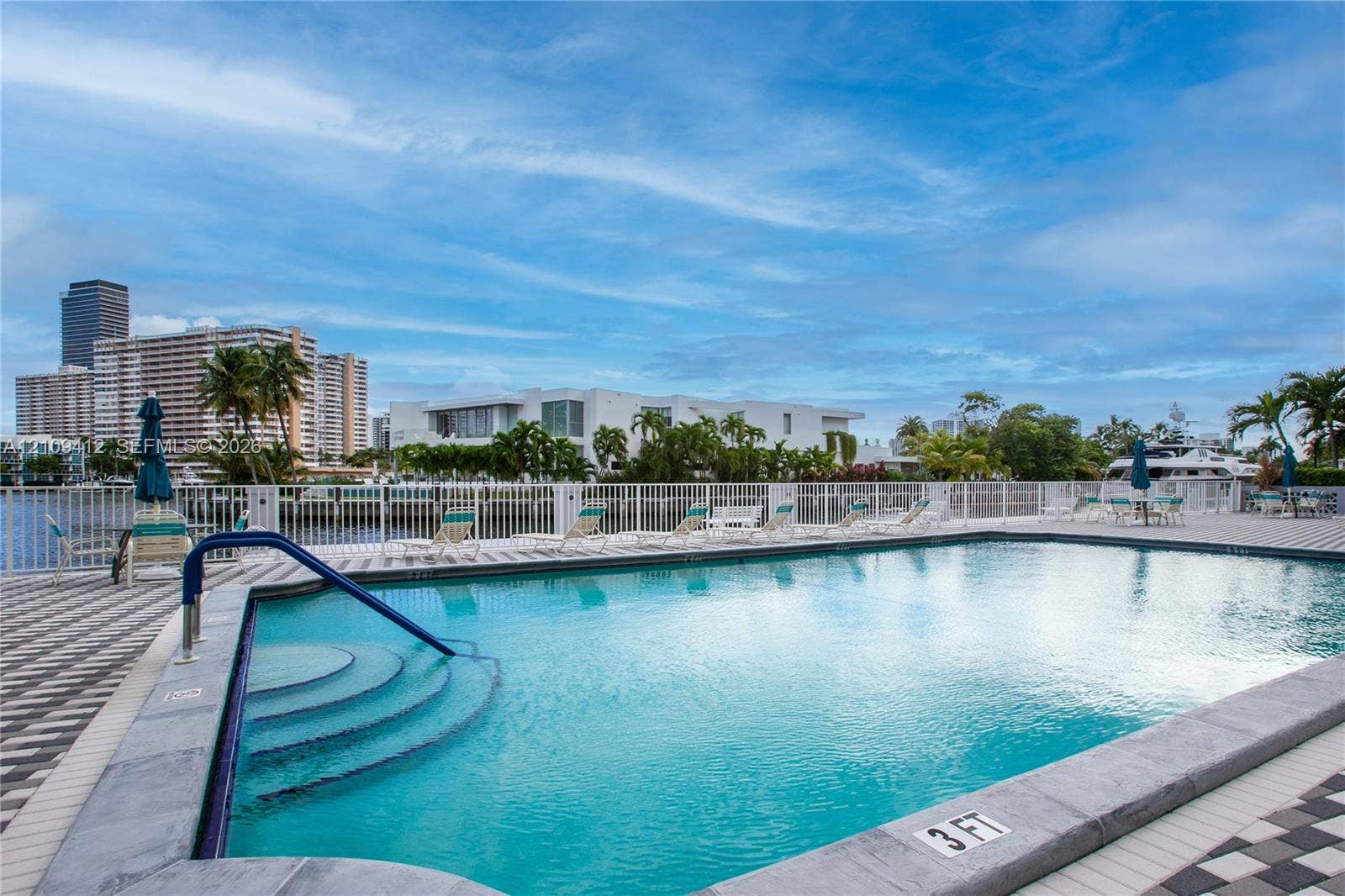 137 Golden Isles Drive, #408, Hallandale Beach, FL 33009 Swimming pool with concrete coping, integrated stairs, and a metal handrail, surrounded by a paved deck and a perimeter fence