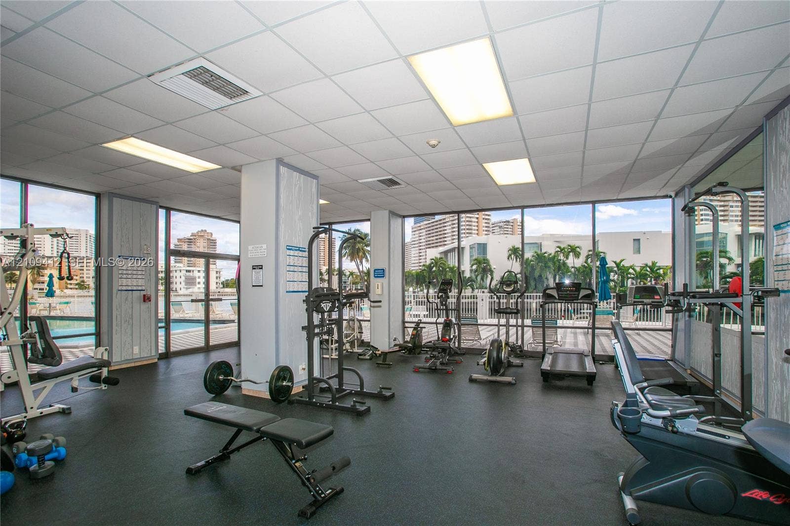137 Golden Isles Drive, #408, Hallandale Beach, FL 33009 Fitness area featuring floor-to-ceiling windows, drop-tile ceiling with recessed lighting, and wall-to-wall rubberized flooring