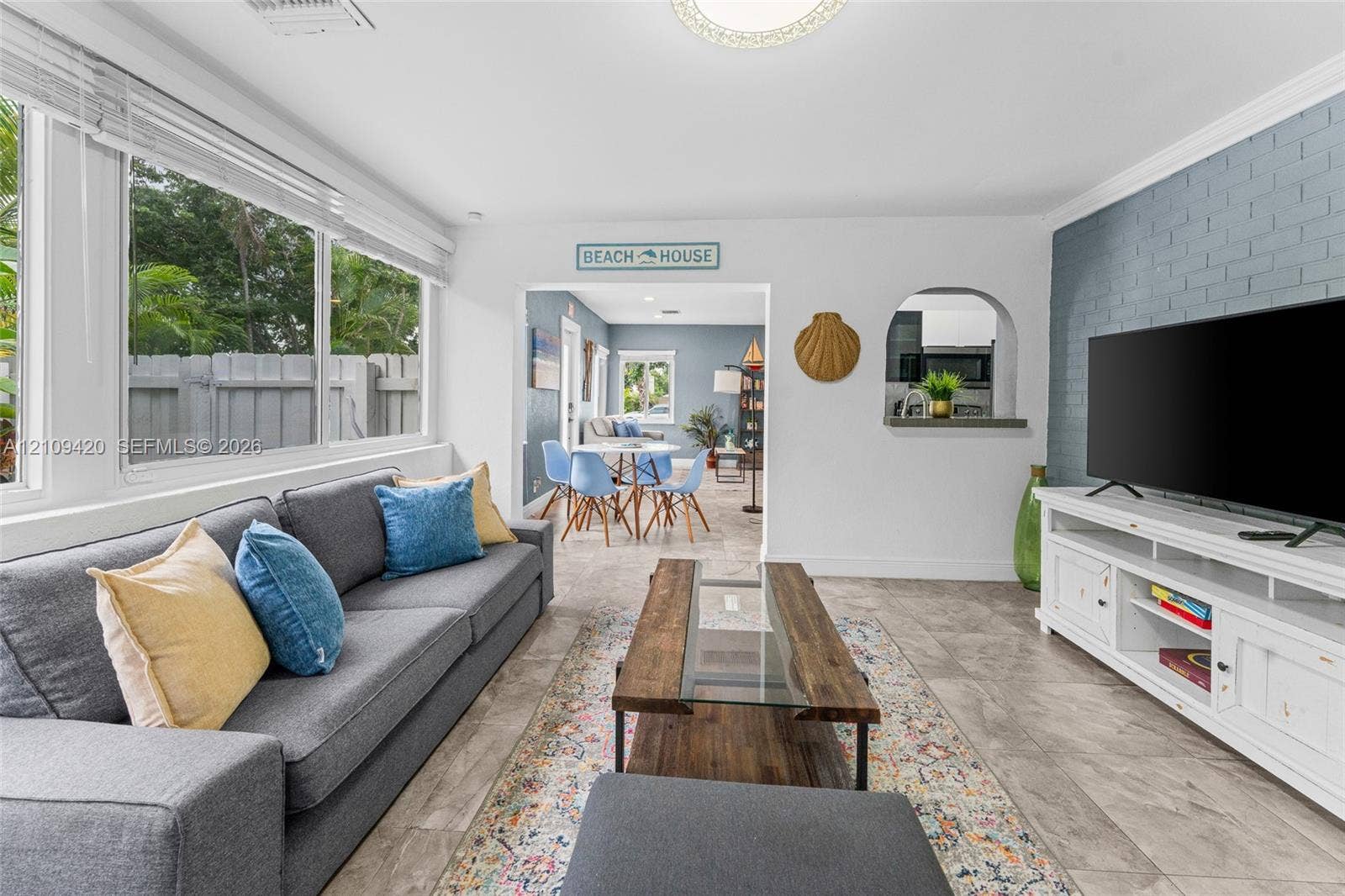 1955 Thomas Street, Hollywood, FL 33020 Living area featuring large windows, stone-finish tile flooring, a blue painted brick accent wall, and an arched passthrough opening