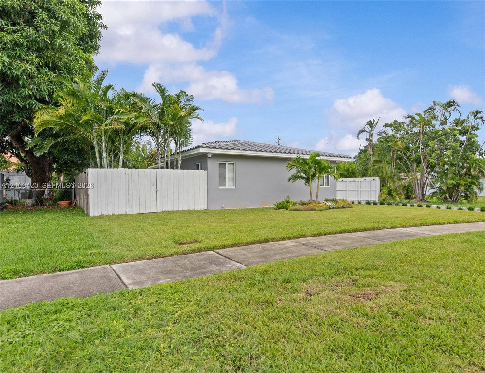 1955 Thomas Street, Hollywood, FL 33020 Exterior featuring a stucco facade, tile roofing, concrete sidewalk, and white fencing, accented by mature palm trees