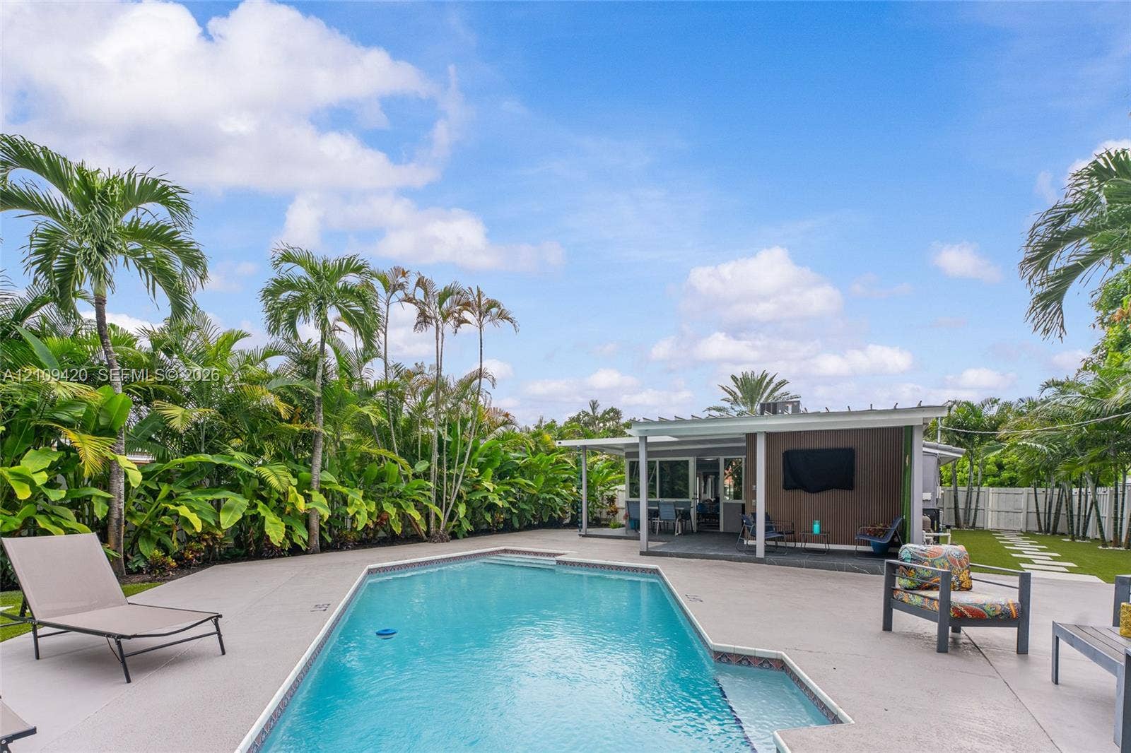 1955 Thomas Street, Hollywood, FL 33020 In-ground swimming pool featuring a shallow sun shelf, expansive concrete deck, covered patio with integrated pergola, and privacy-focused perimeter landscaping