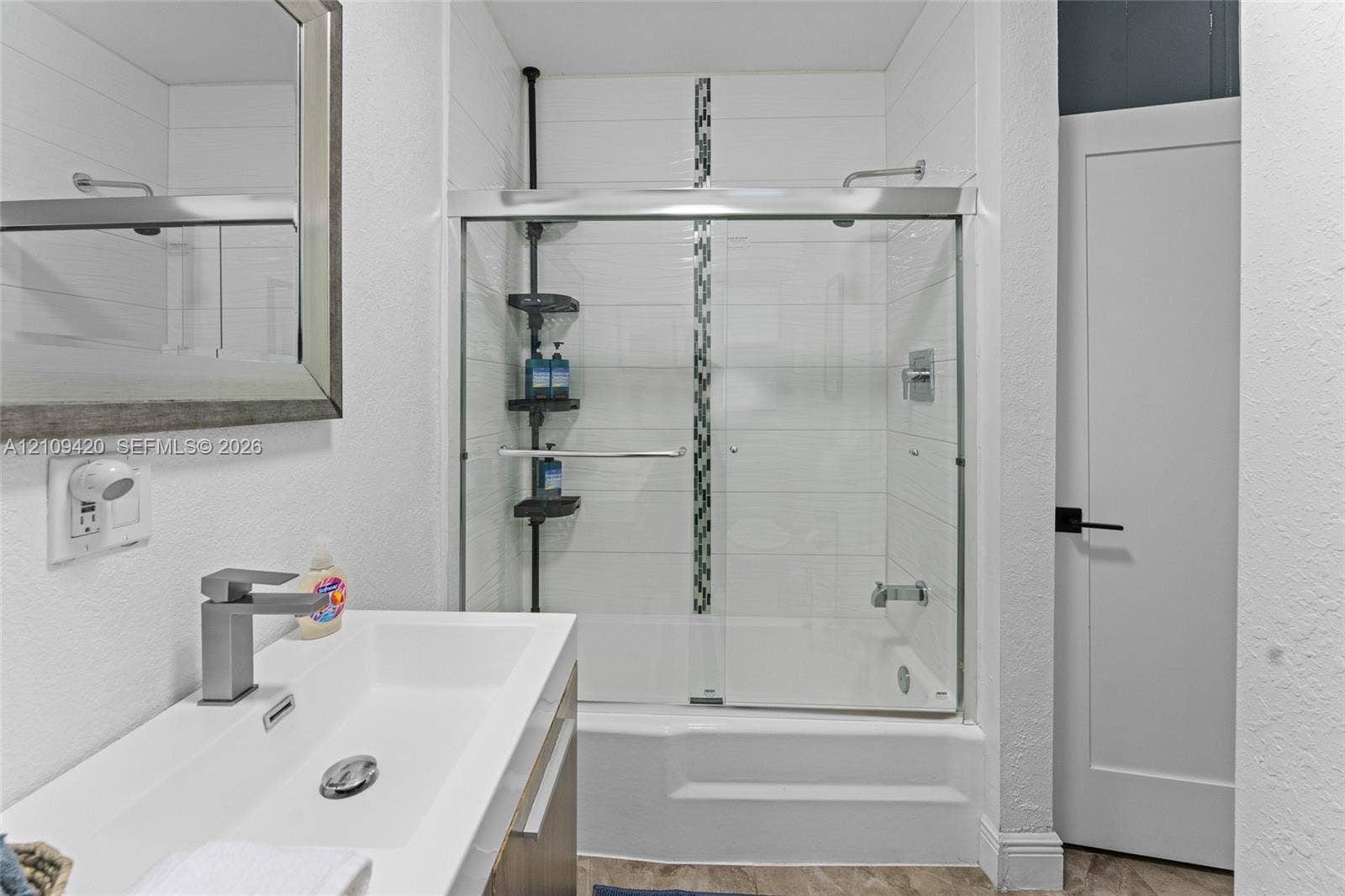 1955 Thomas Street, Hollywood, FL 33020 Modern vanity with a rectangular sink, wall-mounted mirror, glass-enclosed shower and tub combination featuring horizontal tile surrounds and a decorative mosaic accent strip