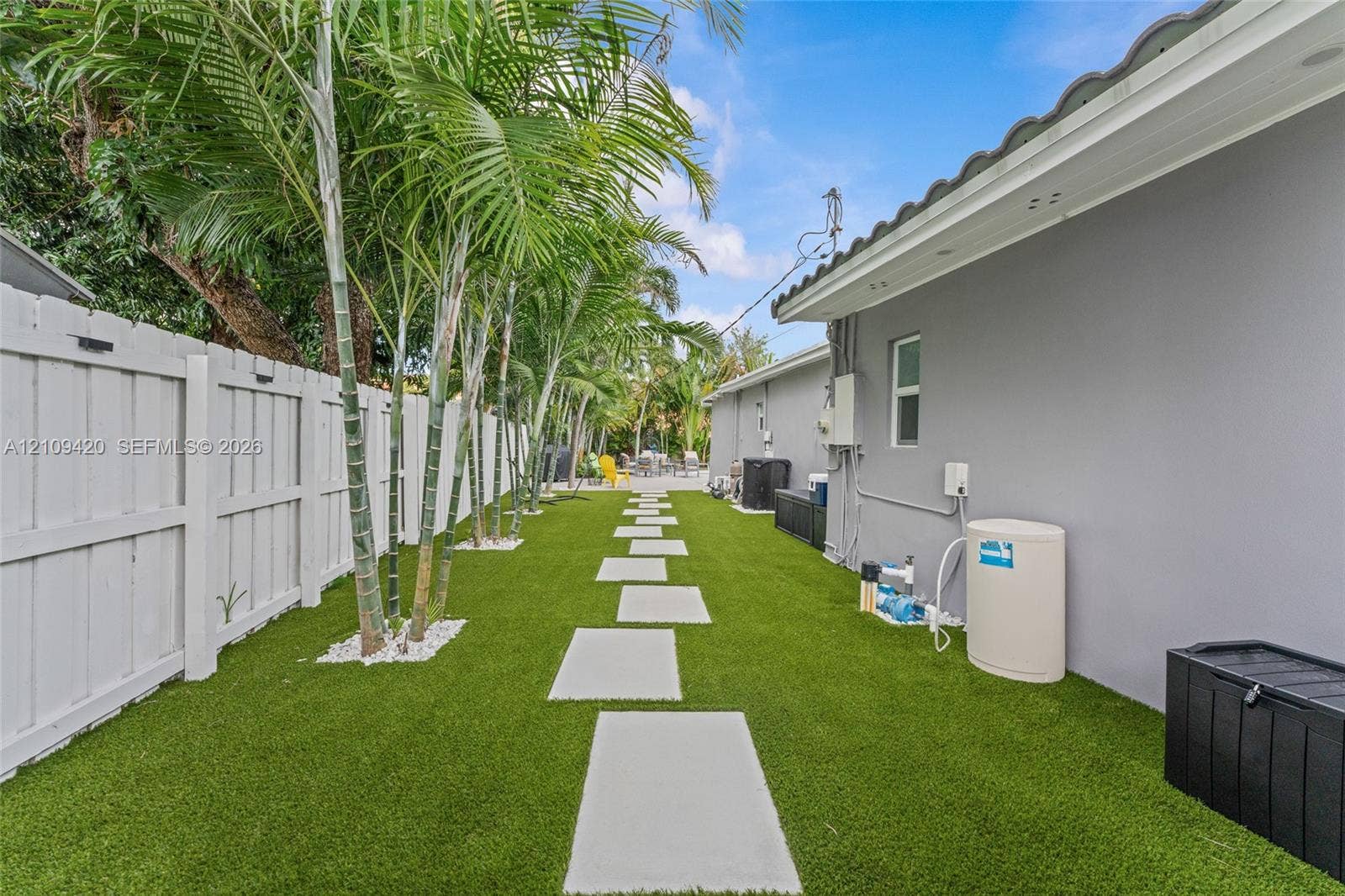 1955 Thomas Street, Hollywood, FL 33020 Side yard featuring synthetic turf, concrete paver pathway, privacy fencing, and mature palm trees