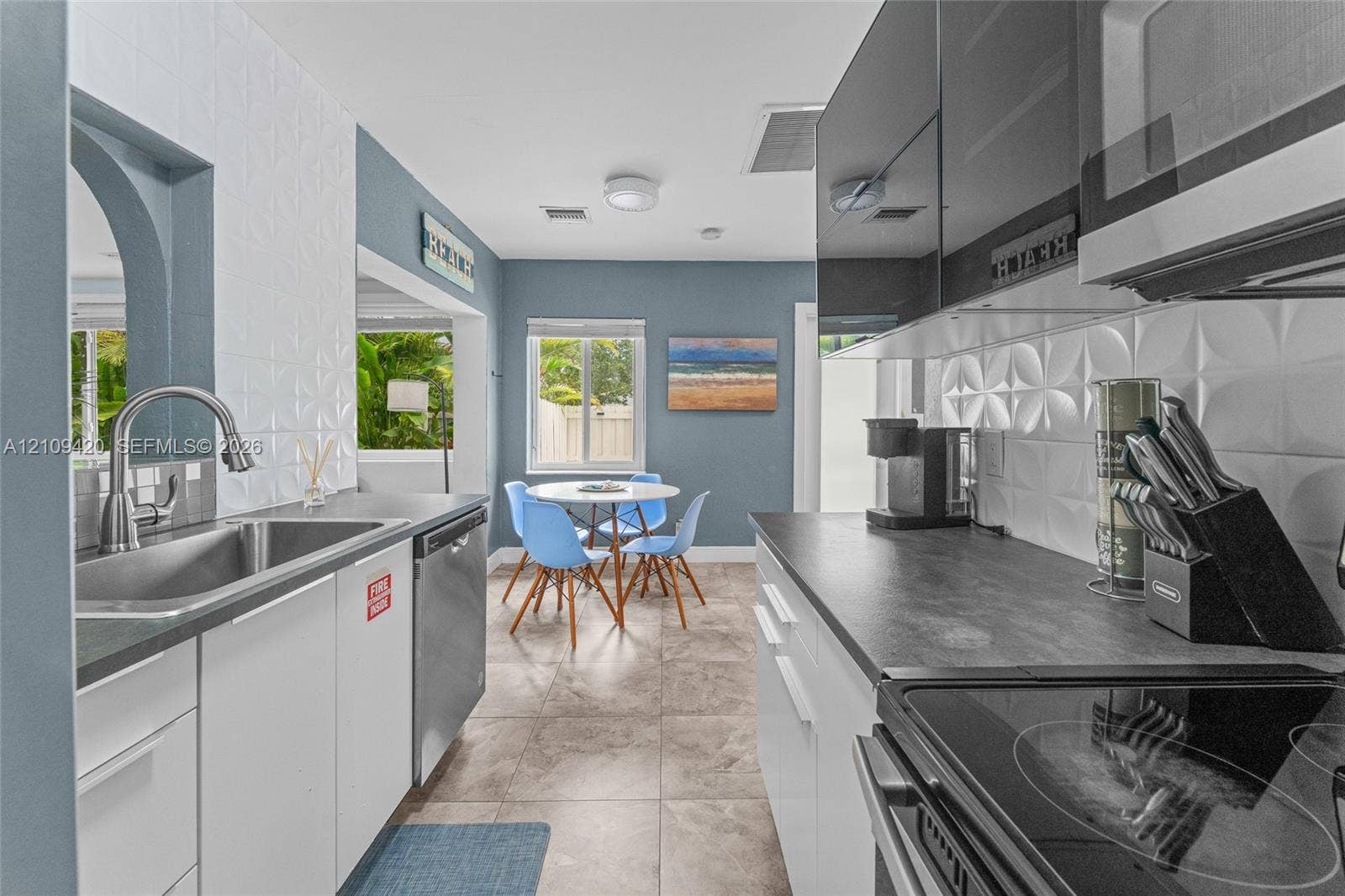 1955 Thomas Street, Hollywood, FL 33020 Kitchen featuring high-gloss black upper cabinetry, white lower cabinets, charcoal-toned countertops, three-dimensional geometric backsplash tile, and stainless-steel appliances