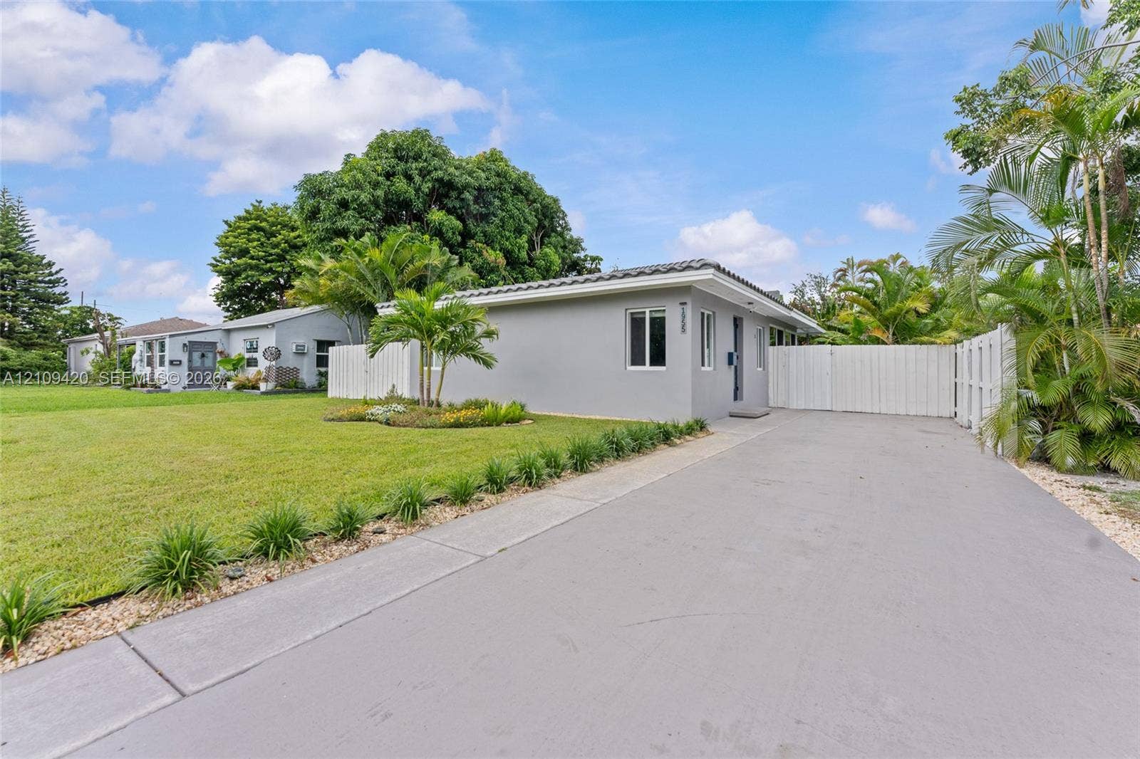 1955 Thomas Street, Hollywood, FL 33020 Single-story exterior featuring a concrete driveway, gated side entrance, manicured lawn, and established tropical landscaping