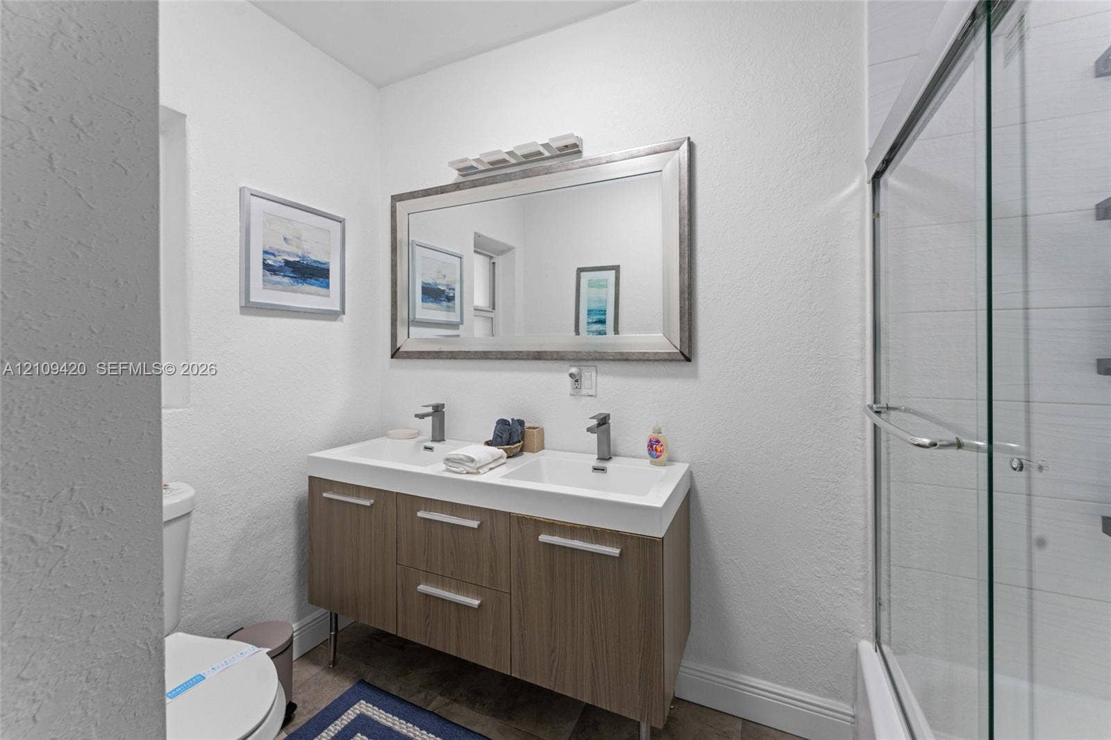 1955 Thomas Street, Hollywood, FL 33020 Floating vanity with a double-basin integrated countertop, metallic hardware, large rectangular wall mirror, and glass-enclosed shower