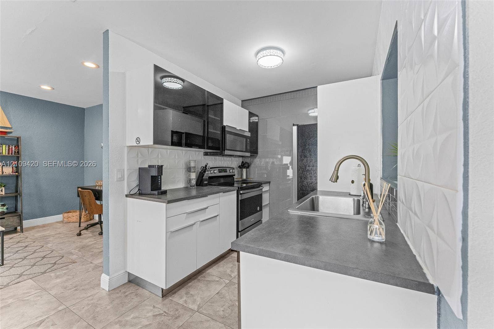 1955 Thomas Street, Hollywood, FL 33020 Kitchen featuring white slab-front cabinetry, dark solid-surface countertops, textured geometric tile backsplash, stainless steel appliances, and a high-arc pull-down faucet