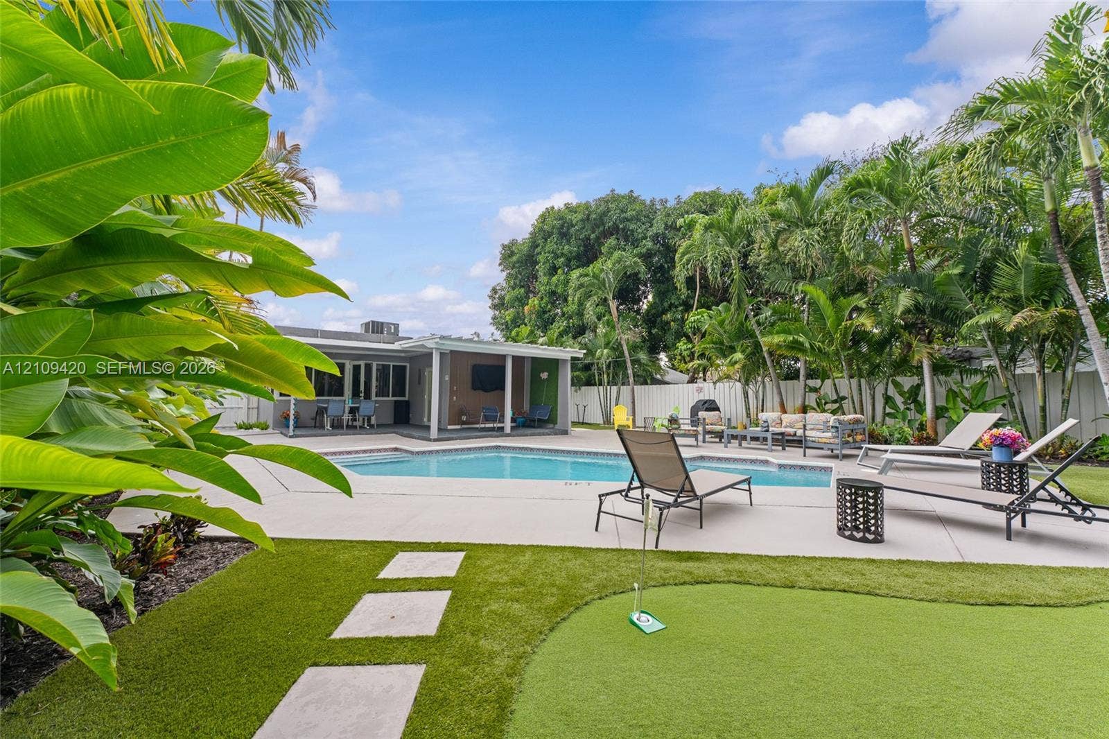 1955 Thomas Street, Hollywood, FL 33020 Backyard featuring an in-ground swimming pool, concrete pool deck, synthetic turf putting green, and mature tropical landscaping