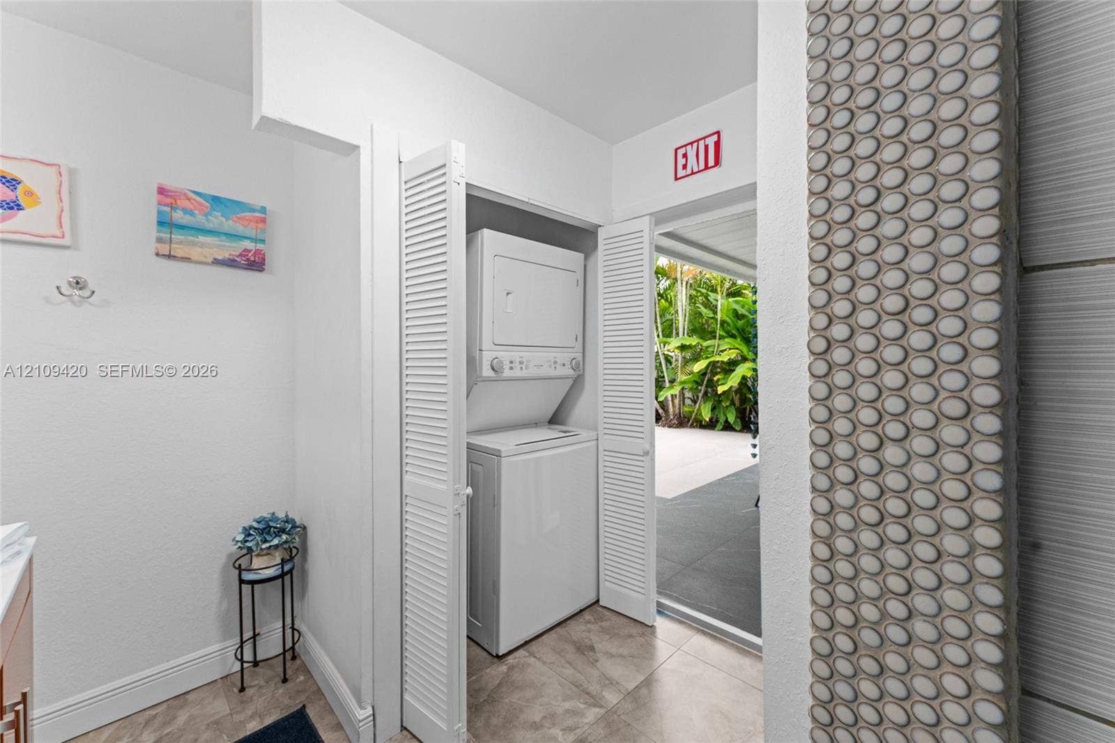1955 Thomas Street, Hollywood, FL 33020 Laundry area featuring a stacked washer and dryer unit concealed behind bi-fold louvered doors, tile flooring, and a decorative circular mosaic tile accent wall