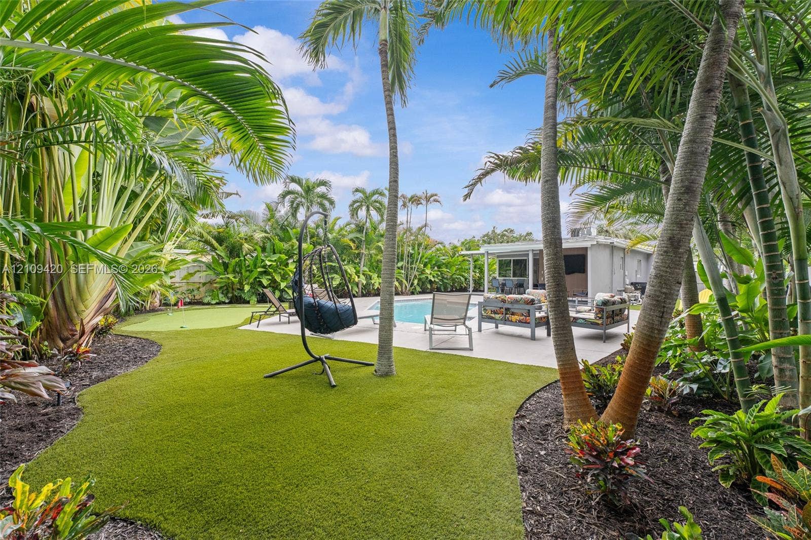 1955 Thomas Street, Hollywood, FL 33020 Backyard featuring a swimming pool, concrete patio, synthetic turf lawn, putting green, and mature palm trees
