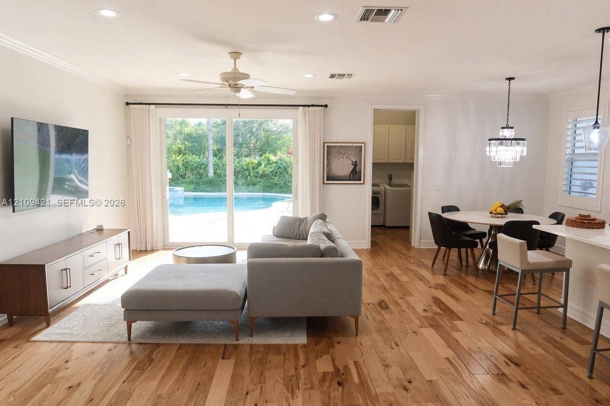 Open-concept living space featuring wood-finish flooring, recessed lighting, a ceiling fan, sliding glass doors, and a multi-tiered crystal pendant light