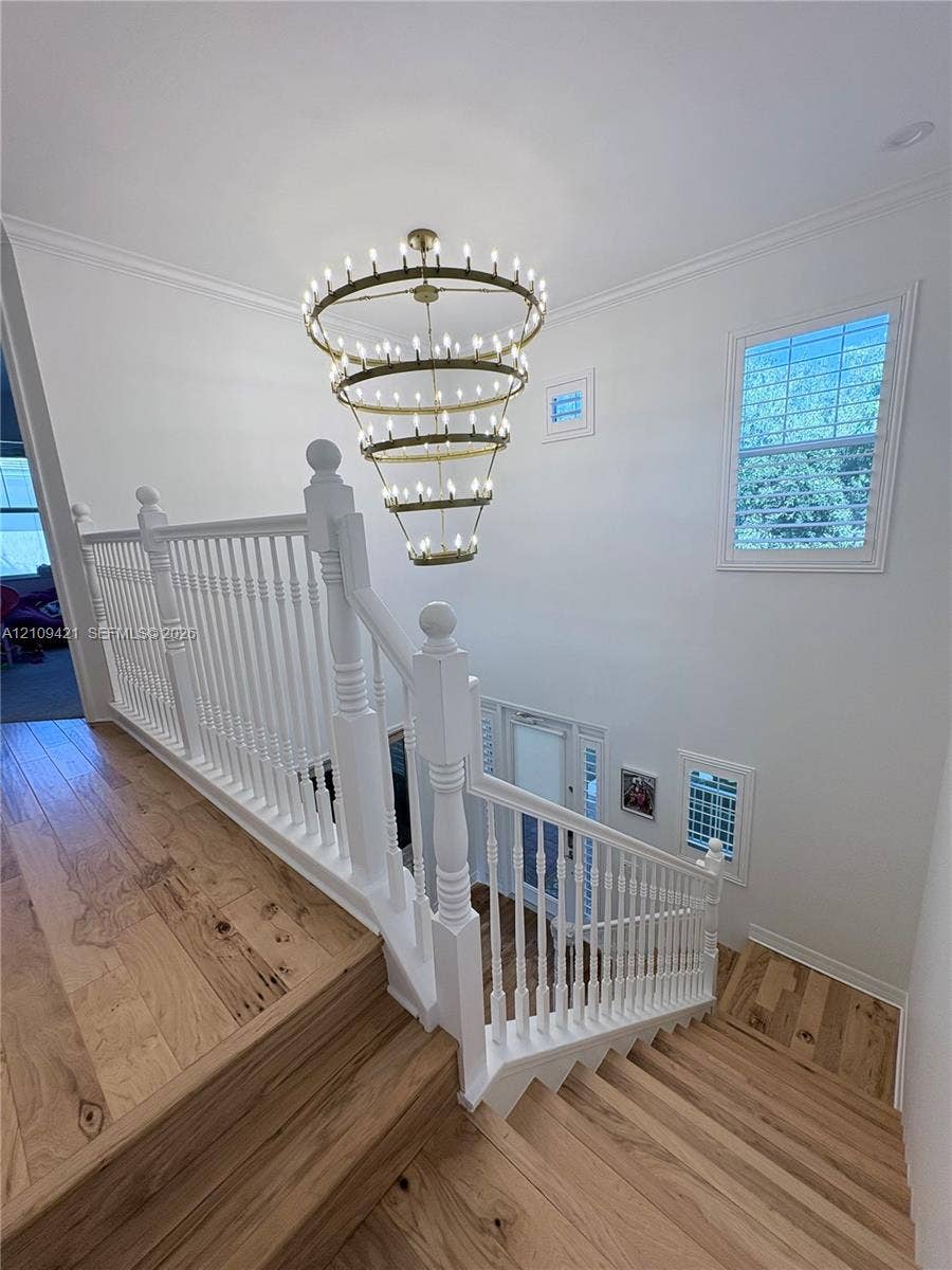 Multi-level staircase featuring wood-finish flooring, a white painted wood railing with detailed balusters, and a tiered brass candelabra chandelier
