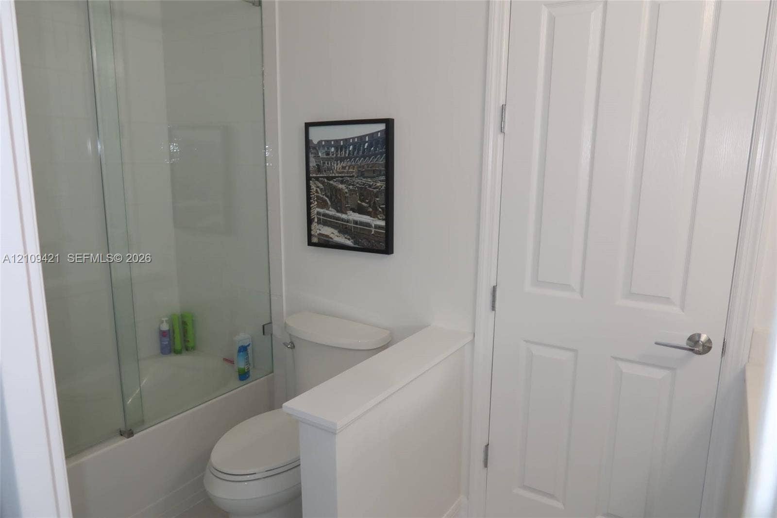 Bathroom featuring a glass shower panel, tub with tiled surround, and a white interior door with brushed metal hardware