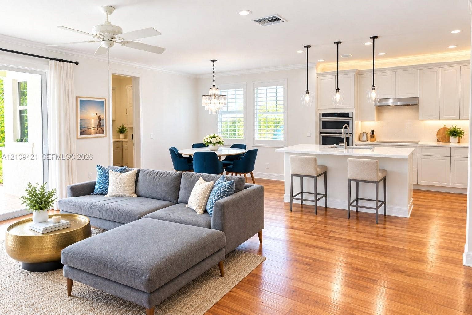 Open-concept interior featuring wood-finish flooring, white cabinetry, an island with stone countertop, stainless steel double wall ovens, and decorative pendant lighting