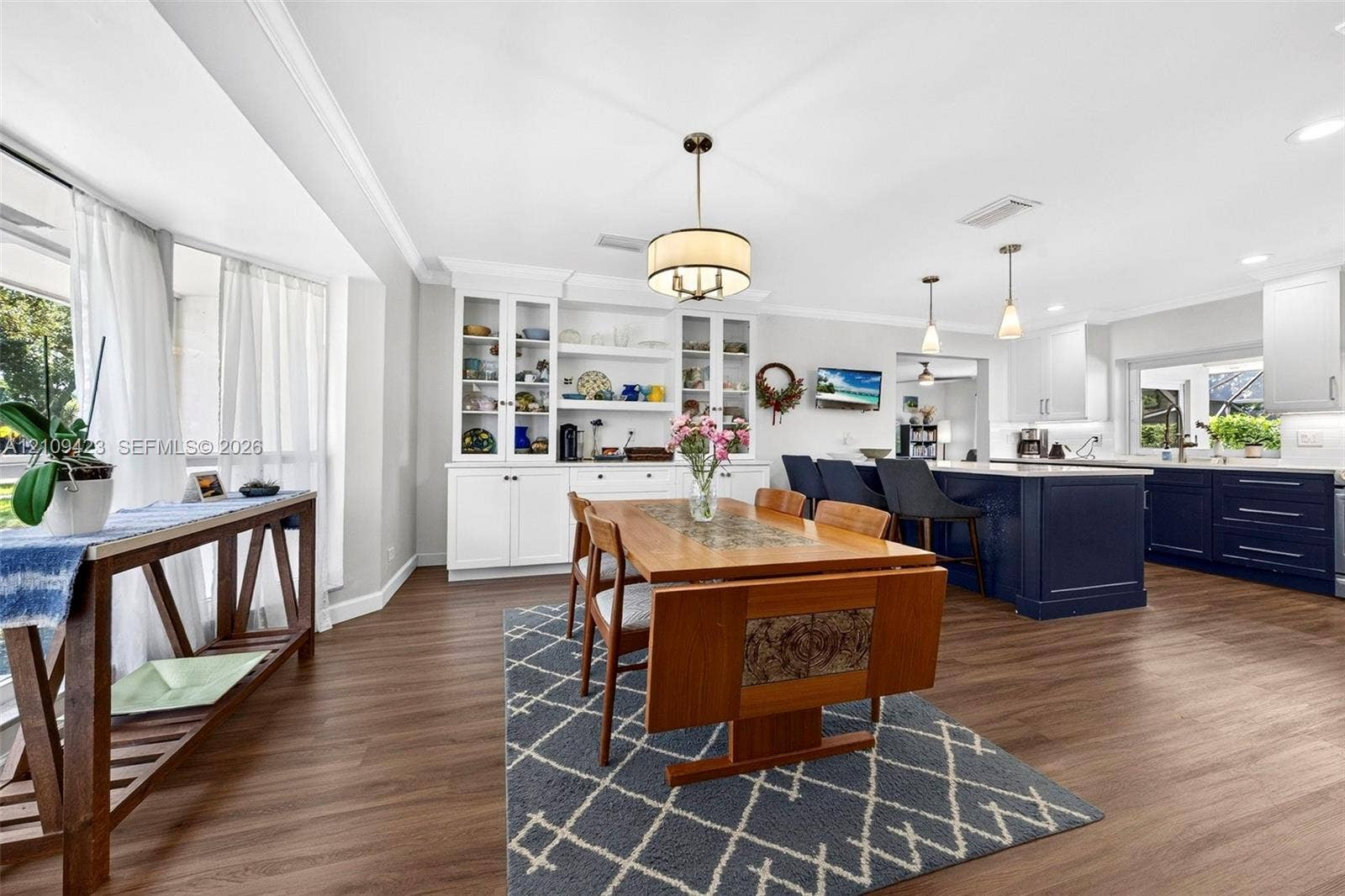 Kitchen featuring white upper cabinetry, a dark-toned center island, built-in display shelving, wood-finish flooring, and recessed lighting