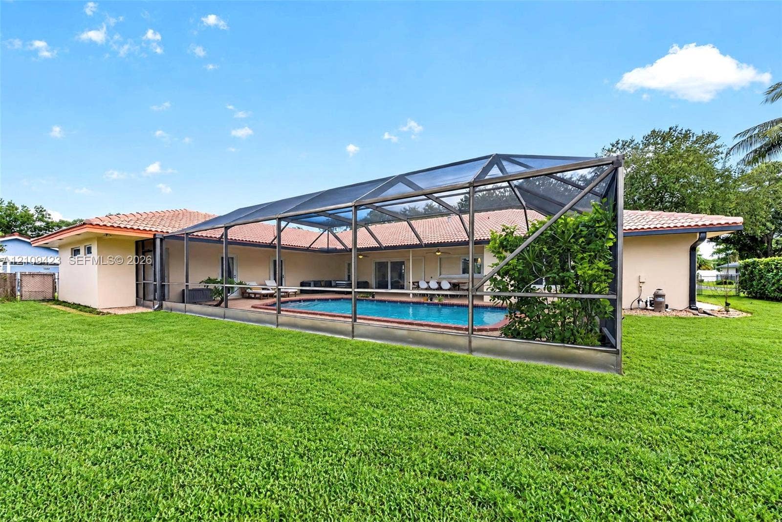 Backyard featuring a screened-in swimming pool enclosure, tile roof, and expansive lawn