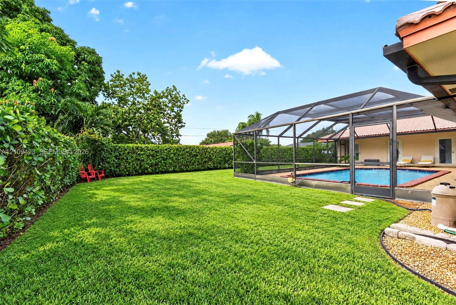 Expansive backyard featuring a screened-in swimming pool, manicured lawn, perimeter hedge, and stone paver path