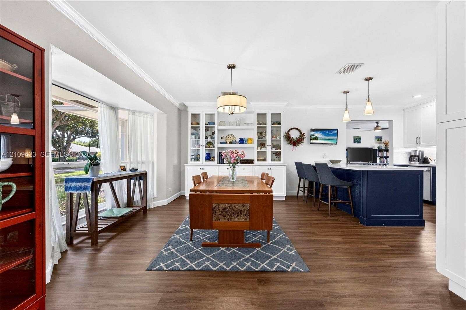 Open concept interior featuring wood-finish flooring, built-in floor-to-ceiling cabinetry, a bay window, a large kitchen island with pendant lighting, and crown molding