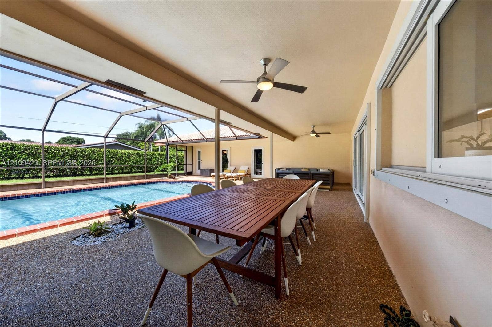 Covered outdoor lanai featuring aggregate flooring, integrated ceiling fans, and a screened enclosure surrounding an in-ground pool