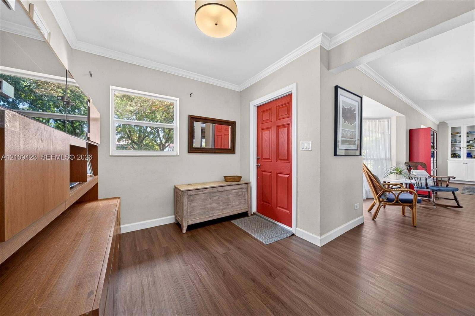 Entryway featuring wood-finish flooring, a six-panel red front door, crown molding, and a built-in cabinetry unit