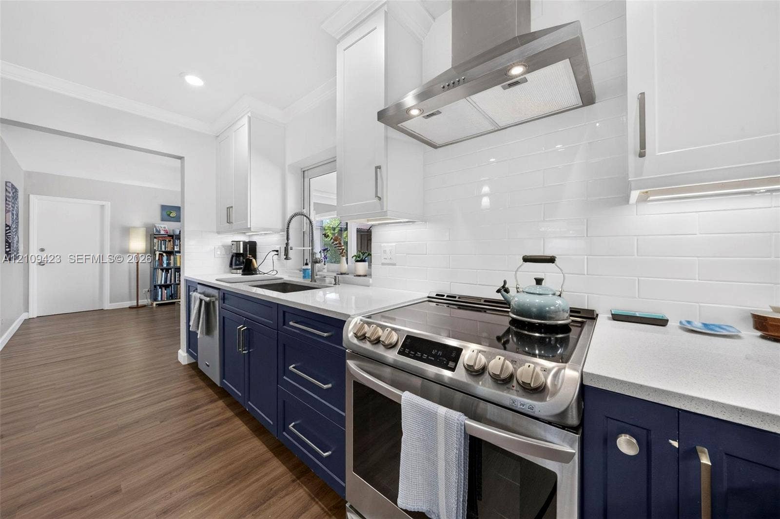 Kitchen featuring navy lower cabinetry, white upper cabinetry, stone-finish countertops, white subway tile backsplash, and stainless steel range hood