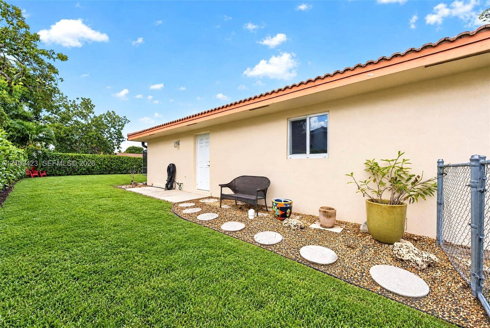 Stucco exterior with a tiled roof, gravel garden bed featuring stone stepping stones, and a grass lawn enclosed by perimeter hedging