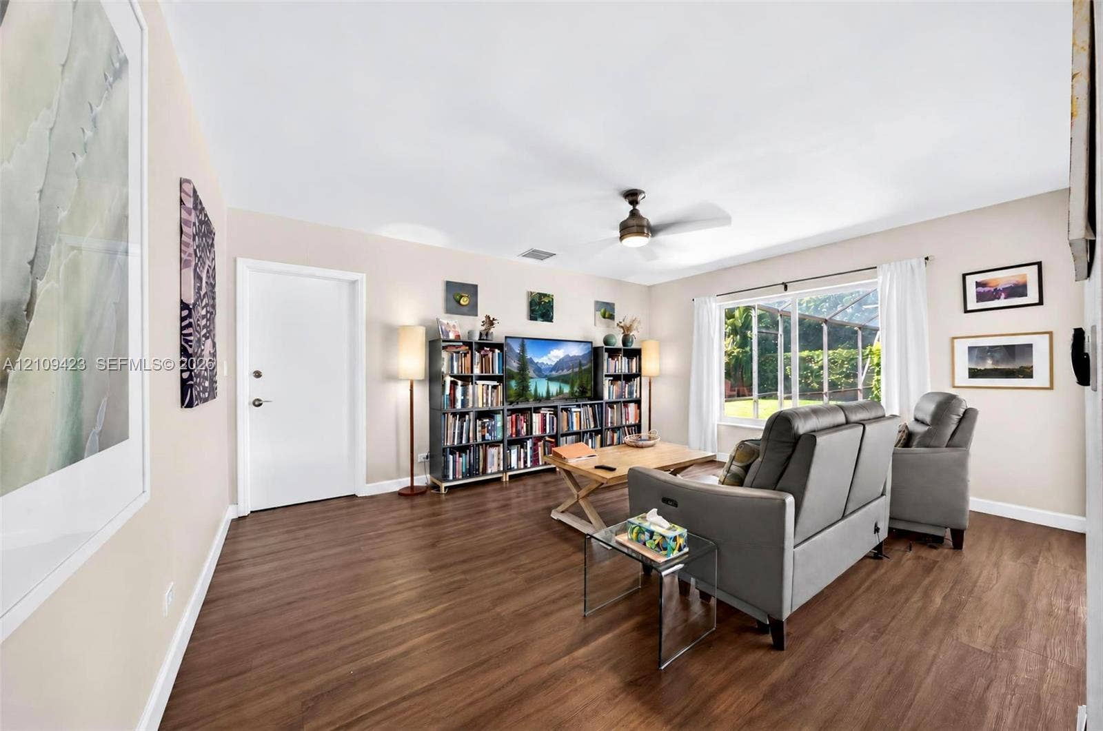 Living area featuring wood-finish flooring, a ceiling fan with integrated lighting, and a large window with natural light