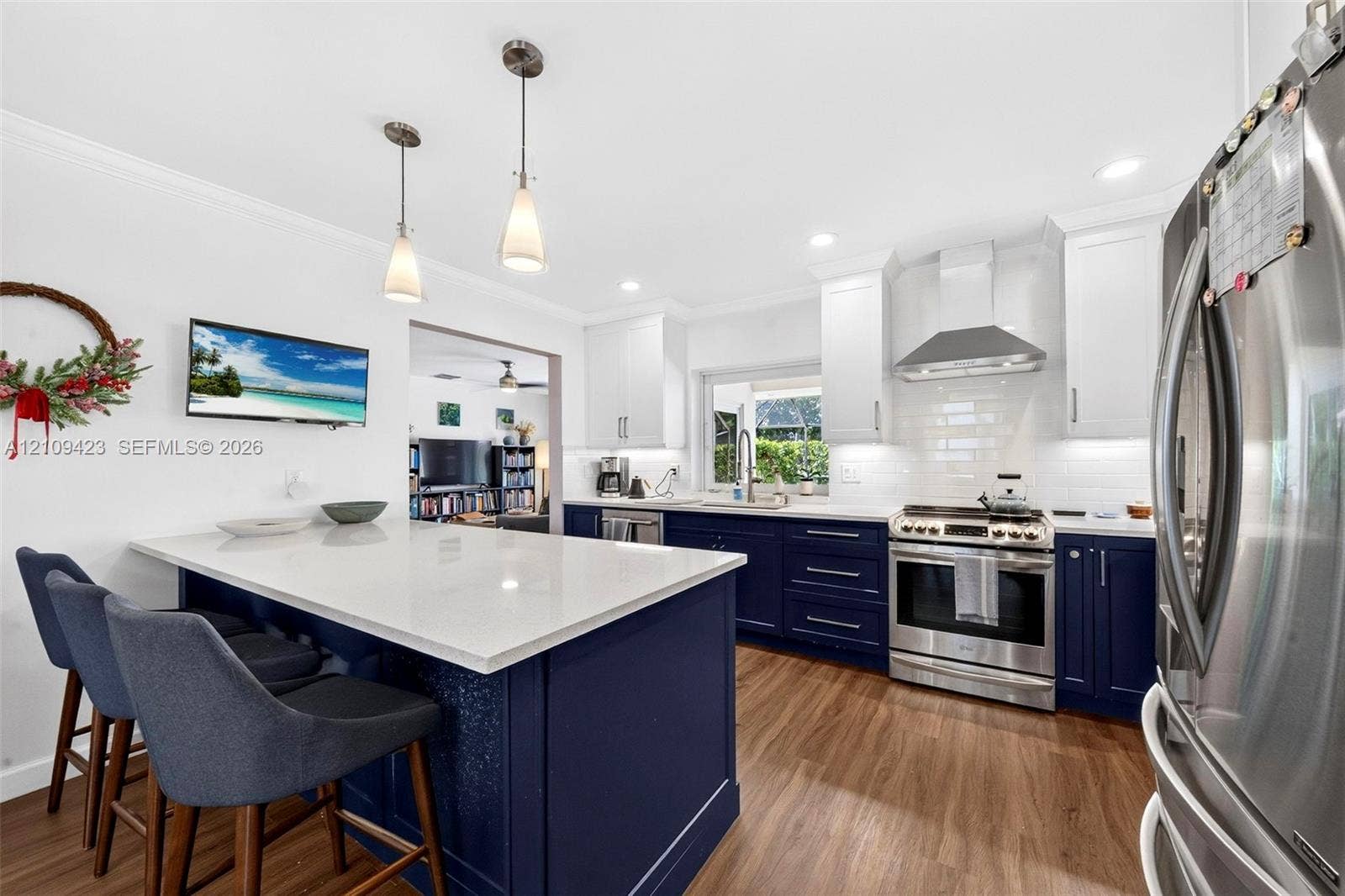 Kitchen featuring dark navy cabinetry, quartz countertops, a central island with dual pendant lighting, stainless steel appliances, and wood-finish flooring