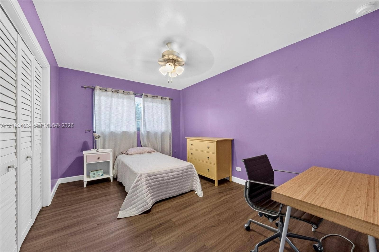 Wood-finish flooring, white louvered-style closet doors, and a ceiling-mounted light fixture with a fan