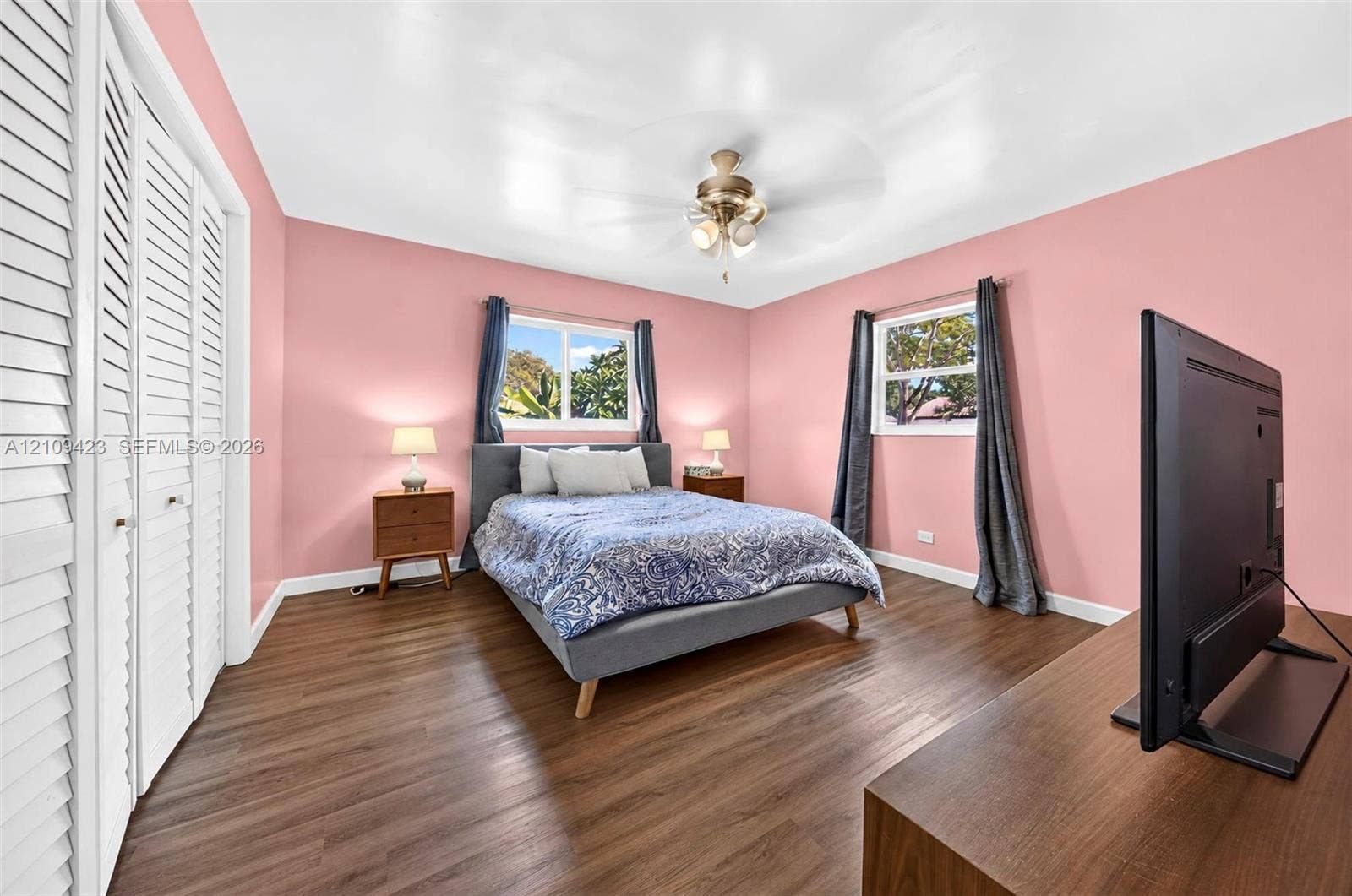 Wood-finish flooring, dual windows, ceiling fan with light fixture, and white louvered closet doors