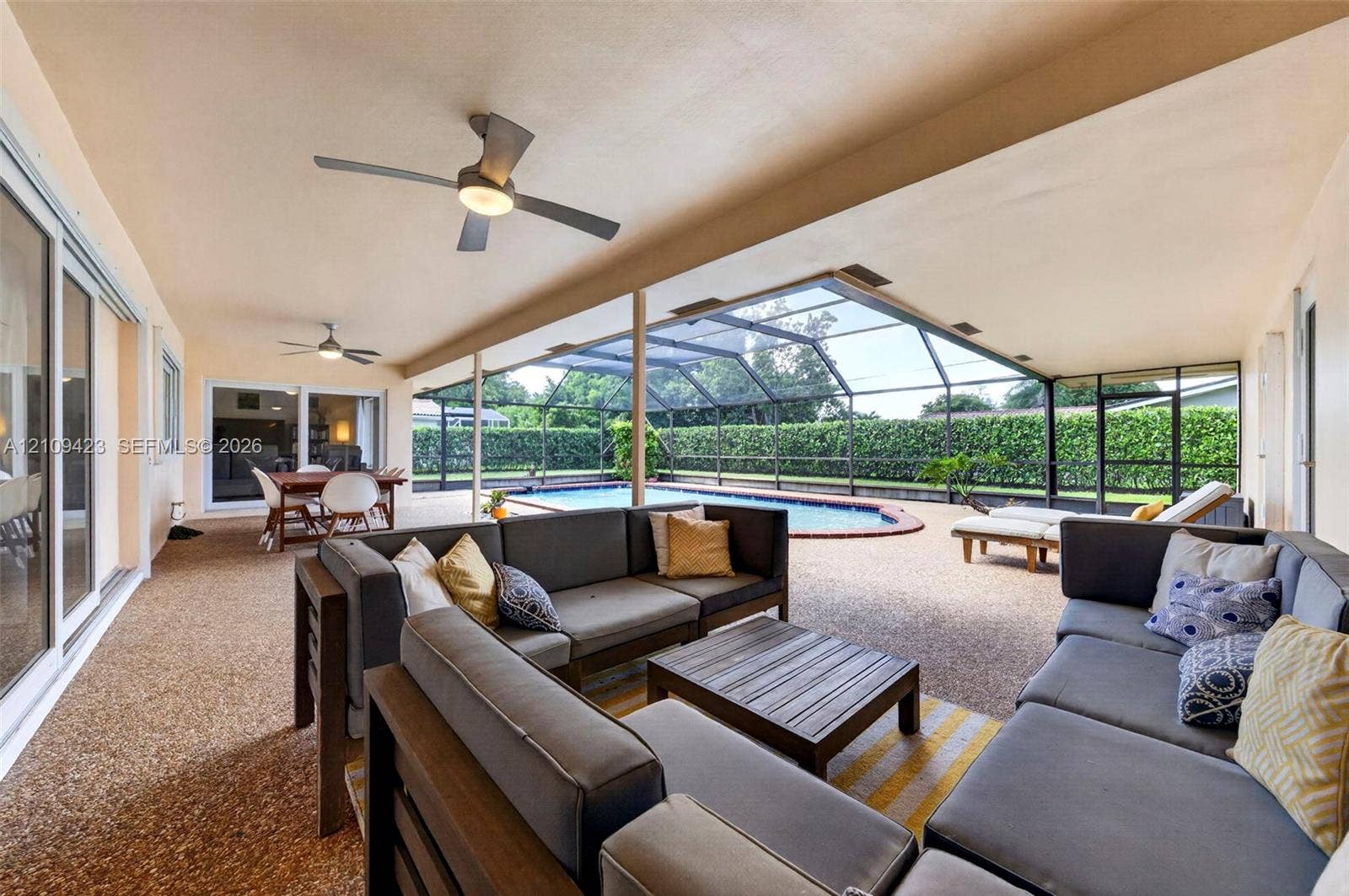 Covered lanai with aggregate flooring, ceiling fans, screened-in enclosure, and pool