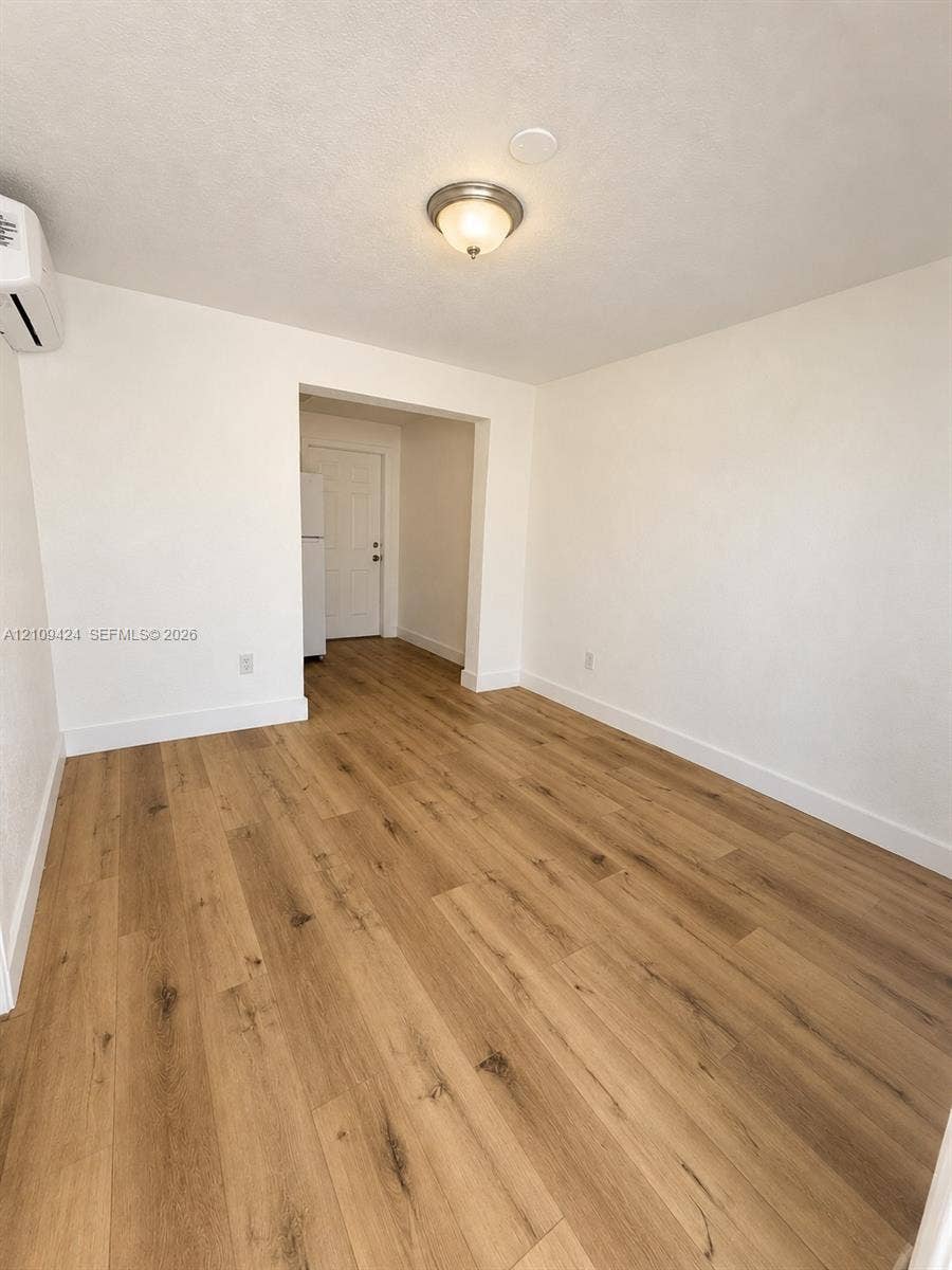 840 NW 10th Street, #5, Hallandale Beach, Hallandale Beach, FL 33009 Interior space featuring neutral wall tones, wood-finish flooring, a wall-mounted ductless climate control unit, and a flush-mount ceiling light fixture