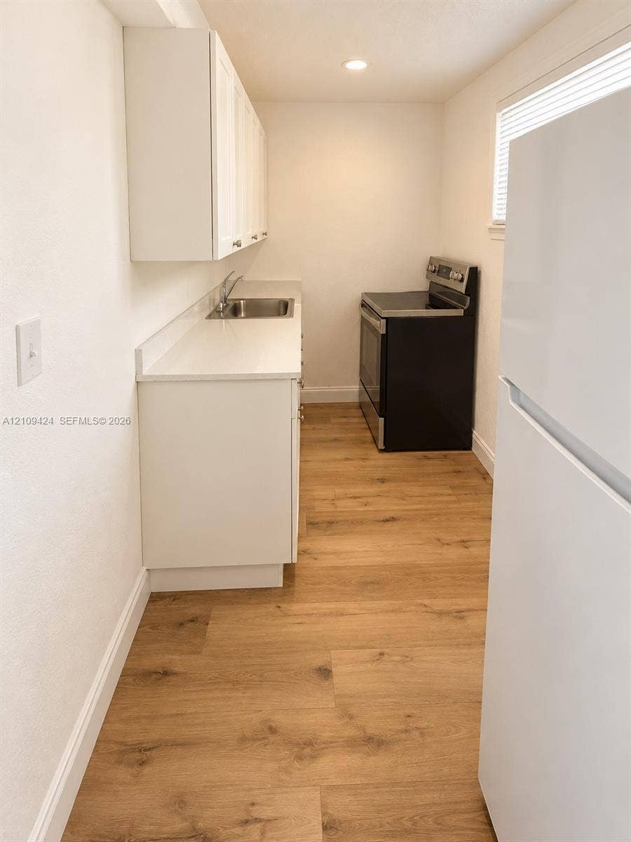 840 NW 10th Street, #5, Hallandale Beach, Hallandale Beach, FL 33009 Galley kitchen featuring white cabinetry, solid-surface countertops, stainless steel sink, wood-finish flooring, and recessed ceiling lighting