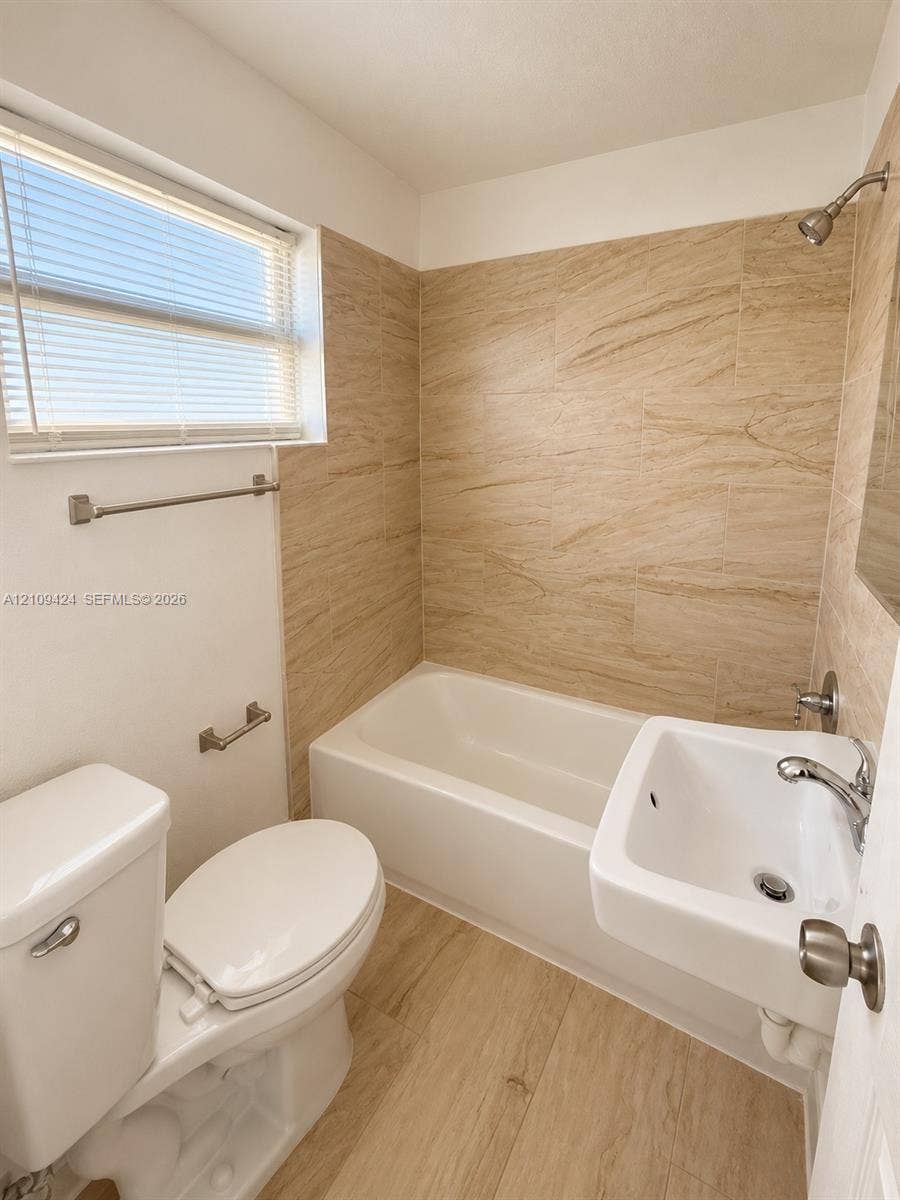 840 NW 10th Street, #5, Hallandale Beach, Hallandale Beach, FL 33009 Bathroom featuring tile-surround bathtub, wall-mounted porcelain sink with chrome faucet, wood-finish flooring, and horizontal-slat window blinds
