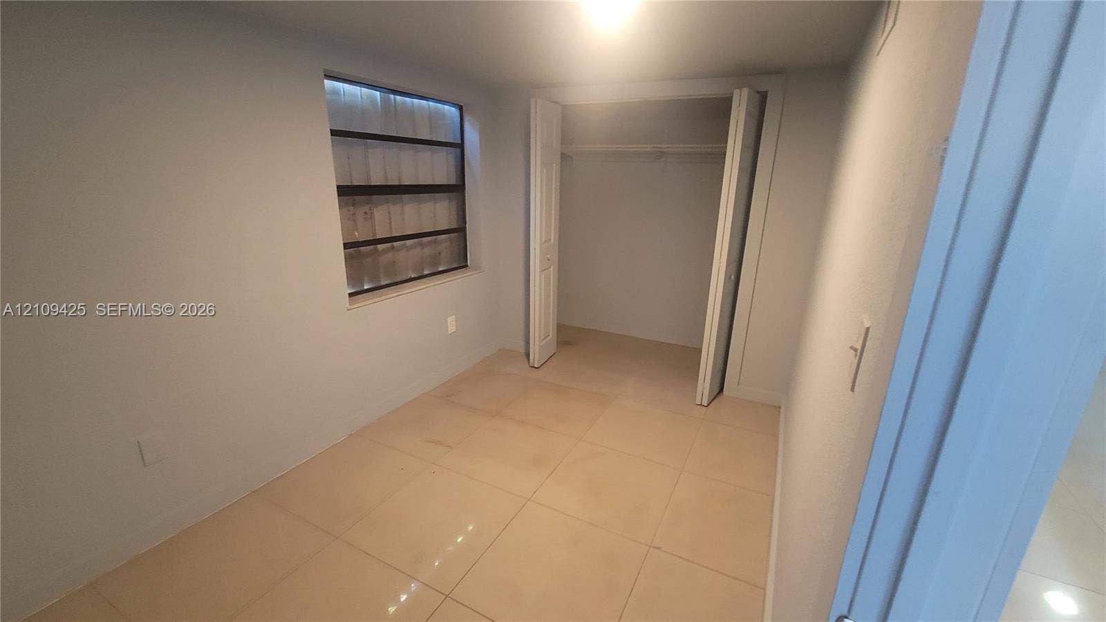 615 NW 25th Court, #B, Miami, Miami, FL 33125 Room featuring large-format ceramic tile flooring, neutral wall paint, a multi-pane jalousie window, and a built-in closet with folding double doors