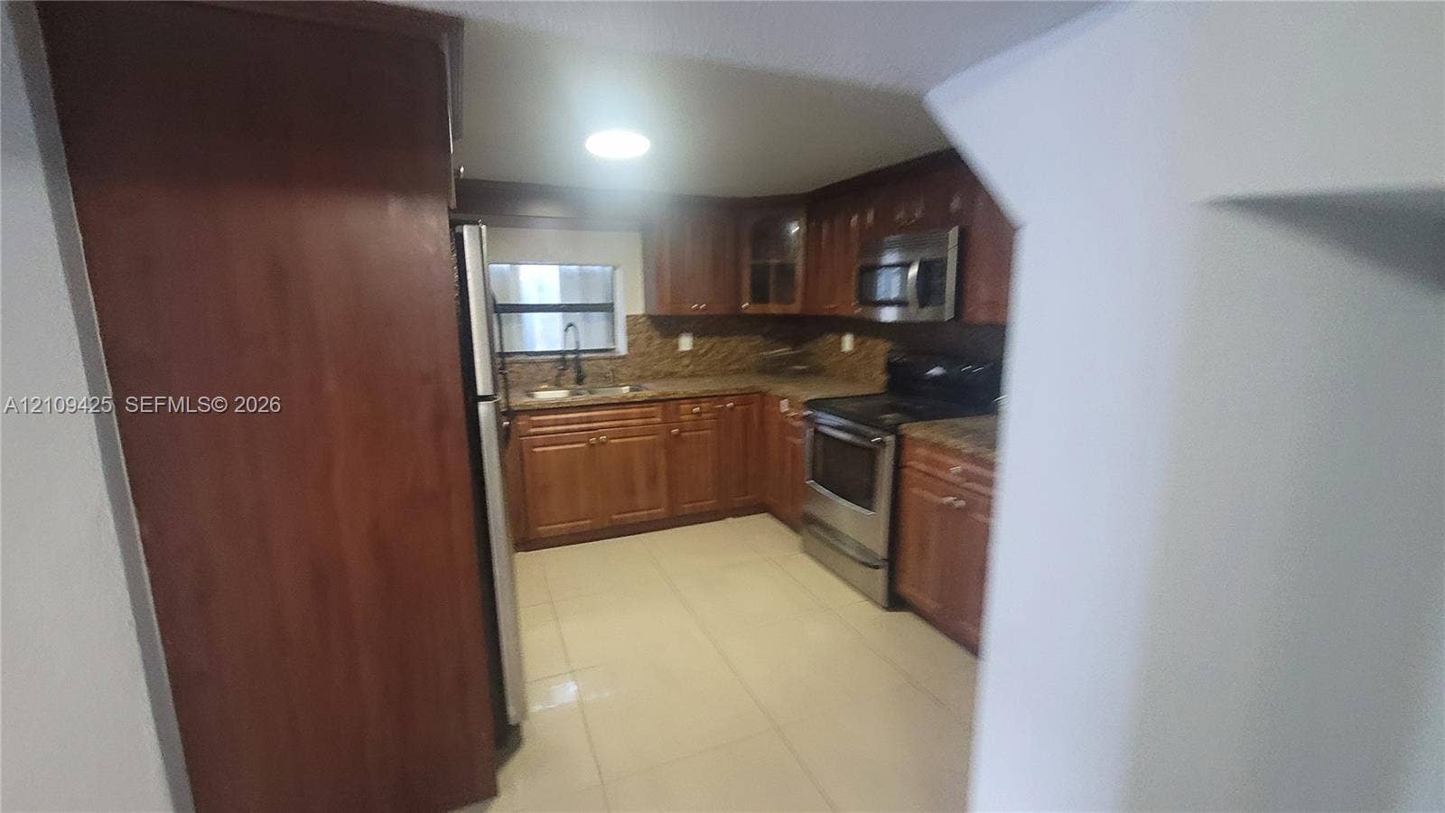615 NW 25th Court, #B, Miami, Miami, FL 33125 Kitchen featuring warm-tone wooden cabinetry, stone-finish countertops, stainless steel appliances, tiled backsplash, and light-tone tile flooring