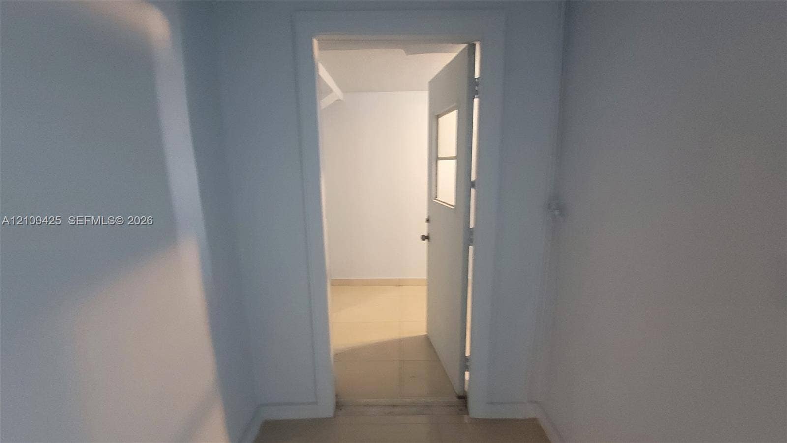 615 NW 25th Court, #B, Miami, Miami, FL 33125 Interior doorway featuring smooth neutral-toned walls, substantial door casing, and a swinging door with a glass pane insert, complemented by light-colored tile flooring